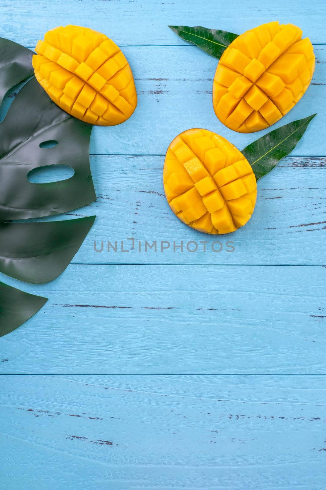 Fresh mango - beautiful chopped fruit with green leaves on bright blue timber background. Tropical fruit design concept. Flat lay. Top view. Copy space by ROMIXIMAGE
