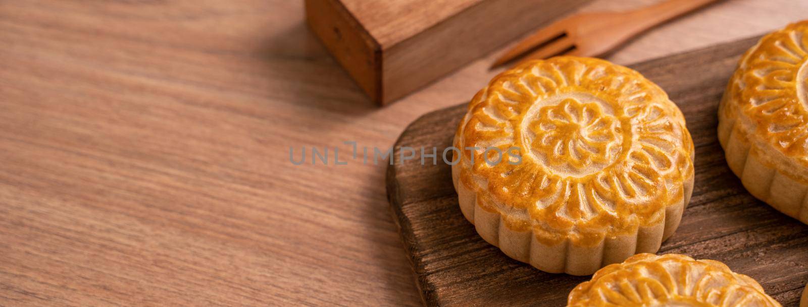 Round shaped moon cake Mooncake - Chinese style traditional pastry during Mid-Autumn Festival / Moon Festival on wooden background and tray, close up by ROMIXIMAGE