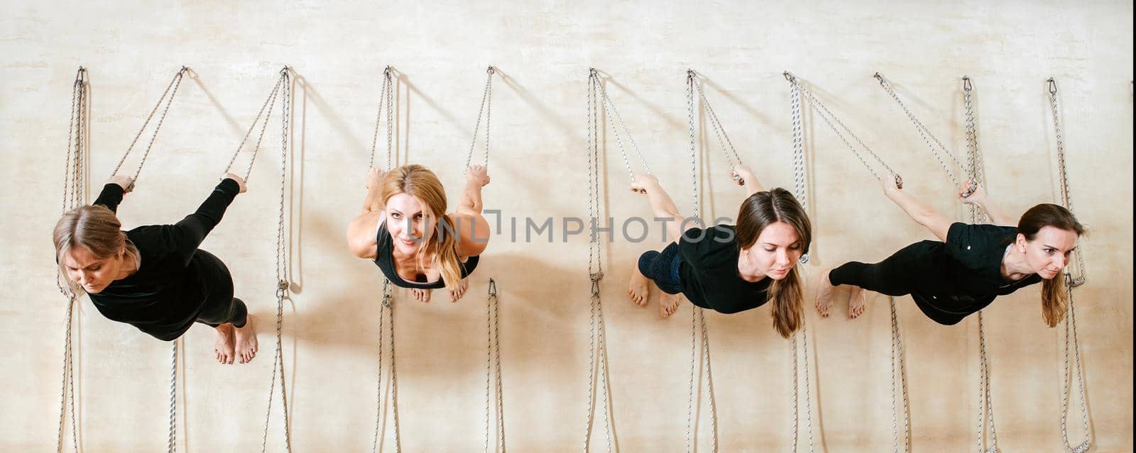 Panorama of lyengar female group of yogi practicing calisthenics exercise in yoga studio hanging on a wall with ropes by Mariakray