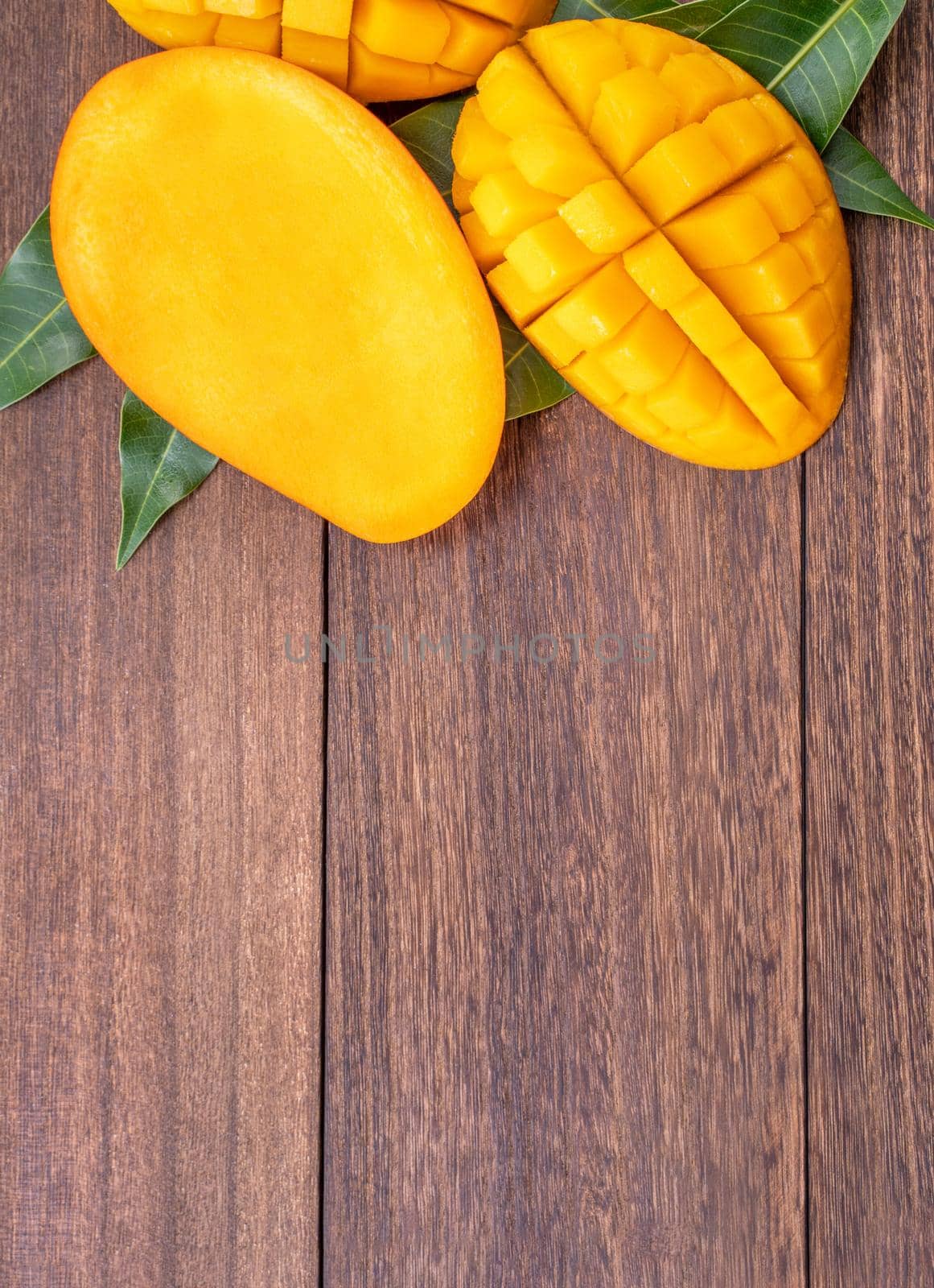 Fresh mango - beautiful chopped fruit with green leaves on dark wooden timber background. Tropical fruit design concept. Flat lay. Top view. Copy space by ROMIXIMAGE