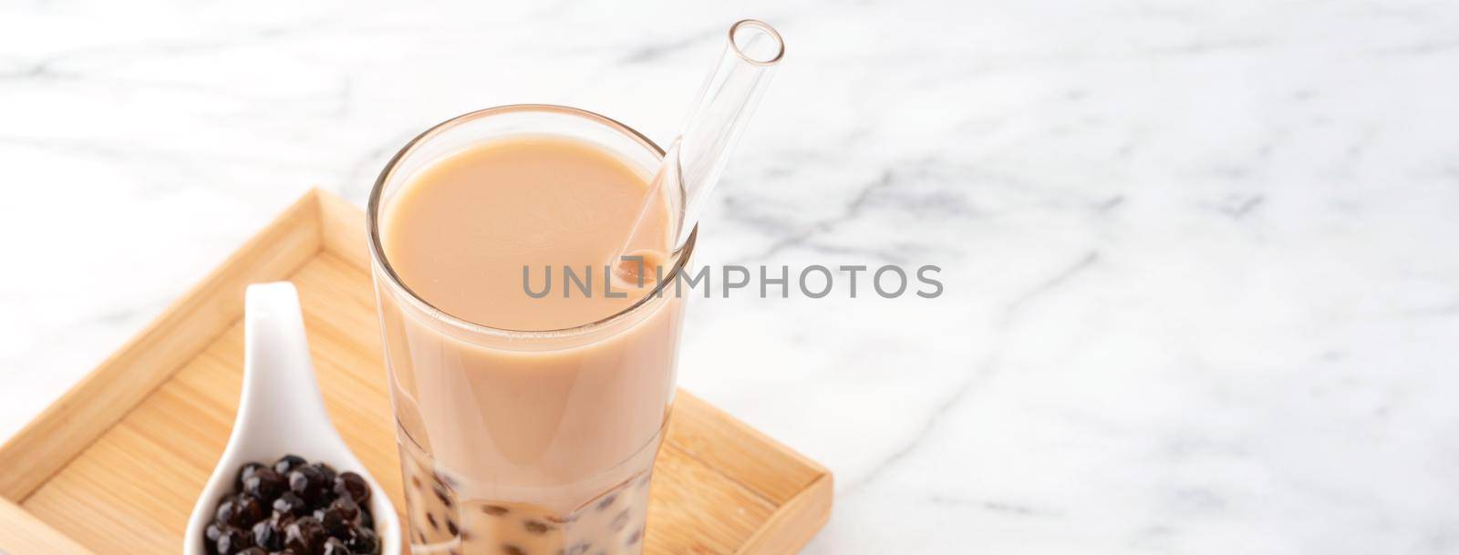 Tapioca pearl ball bubble milk tea, popular Taiwan drink, in drinking glass with straw on marble white table and wooden tray, close up, copy space. by ROMIXIMAGE