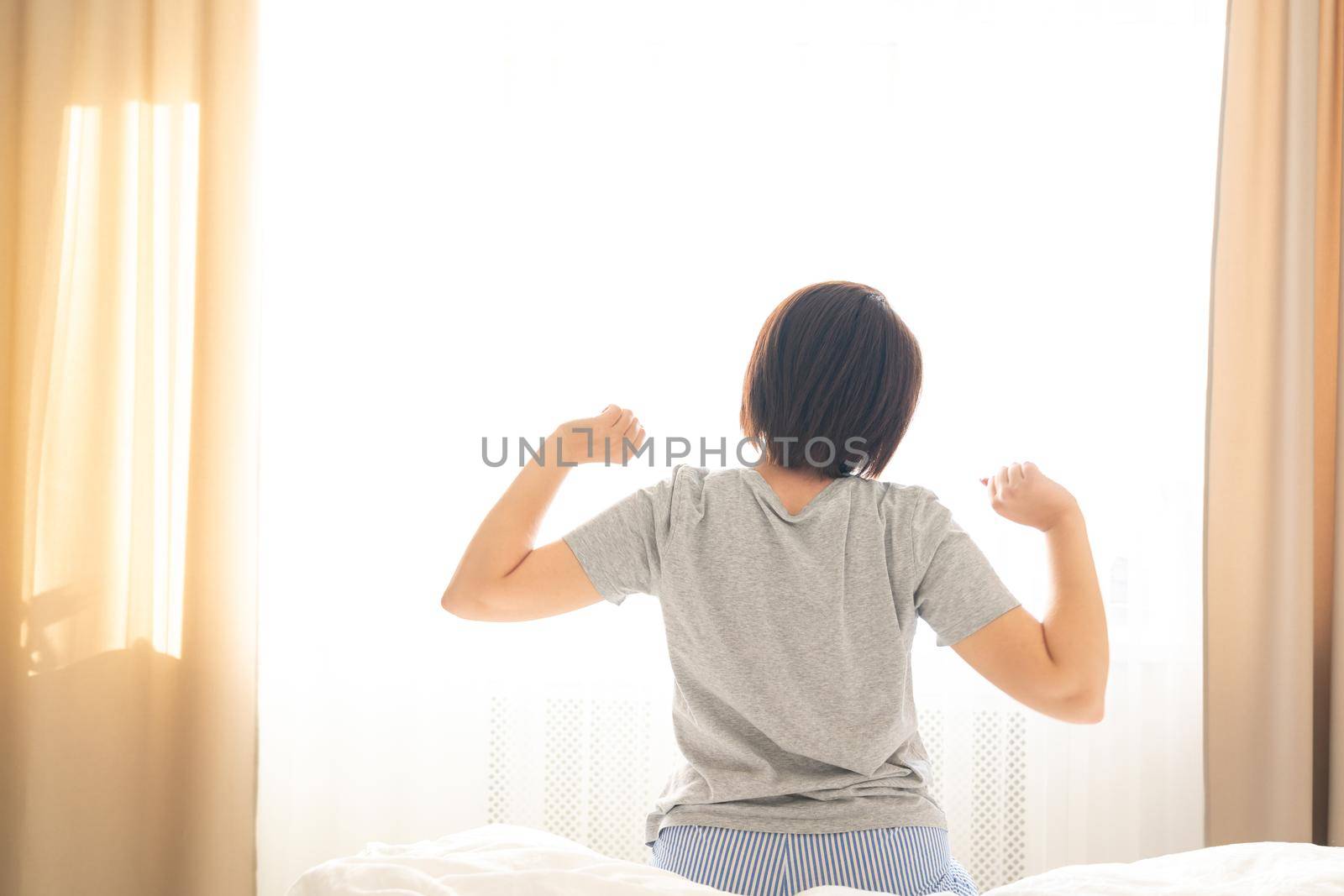 Woman stretching in bed after wake up in front of window, back view by Mariakray