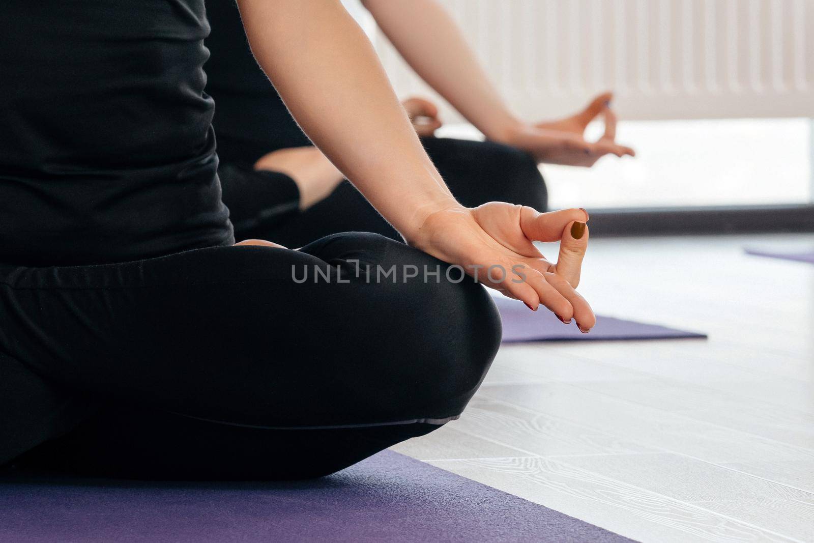 Close up of yoga women sitting in lotus asana during yoga class, cropped view by Mariakray