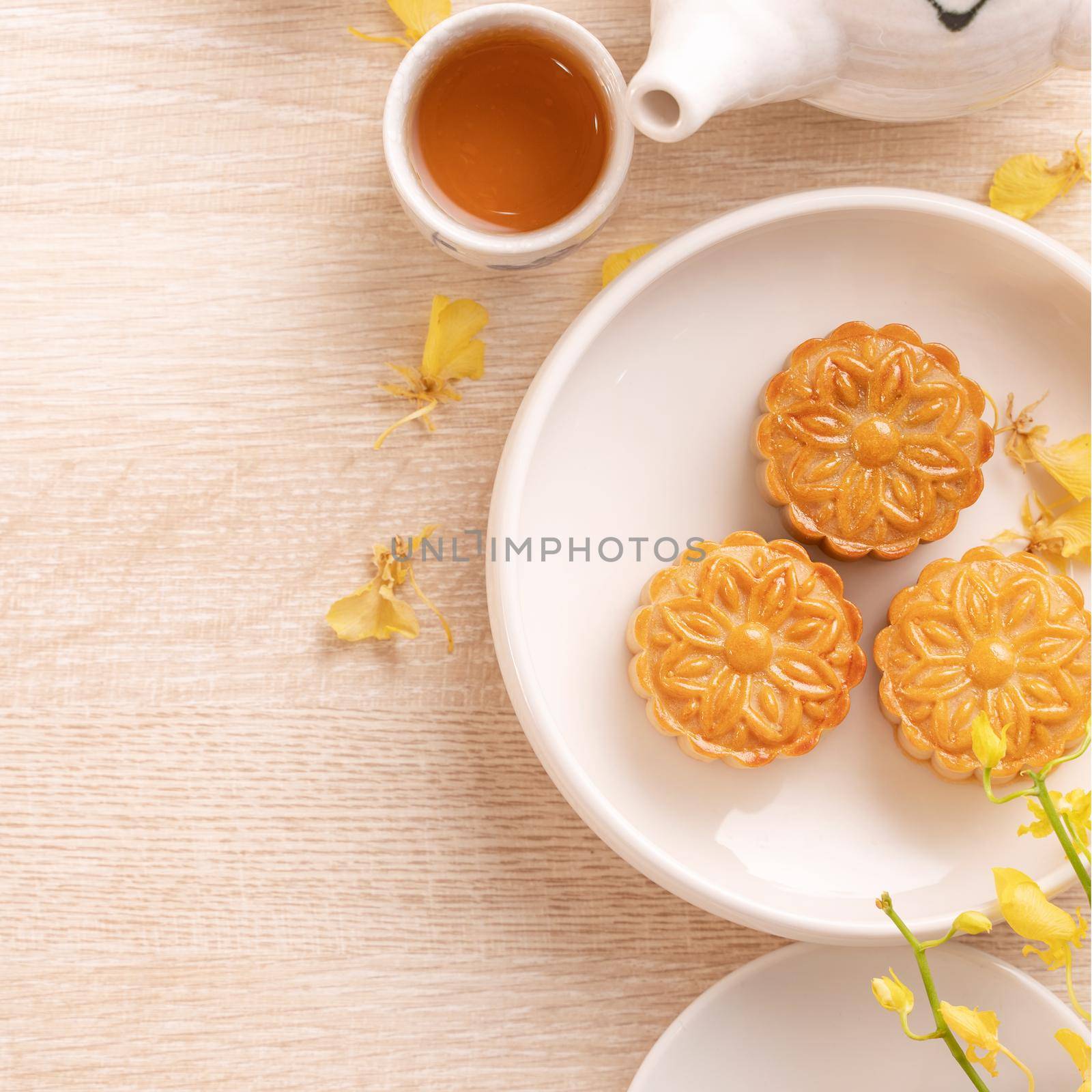 Delicious moon cake for Mid-Autumn festival with beautiful pattern, decorated with yellow flowers and tea. Concept of festive afternoon pastry design