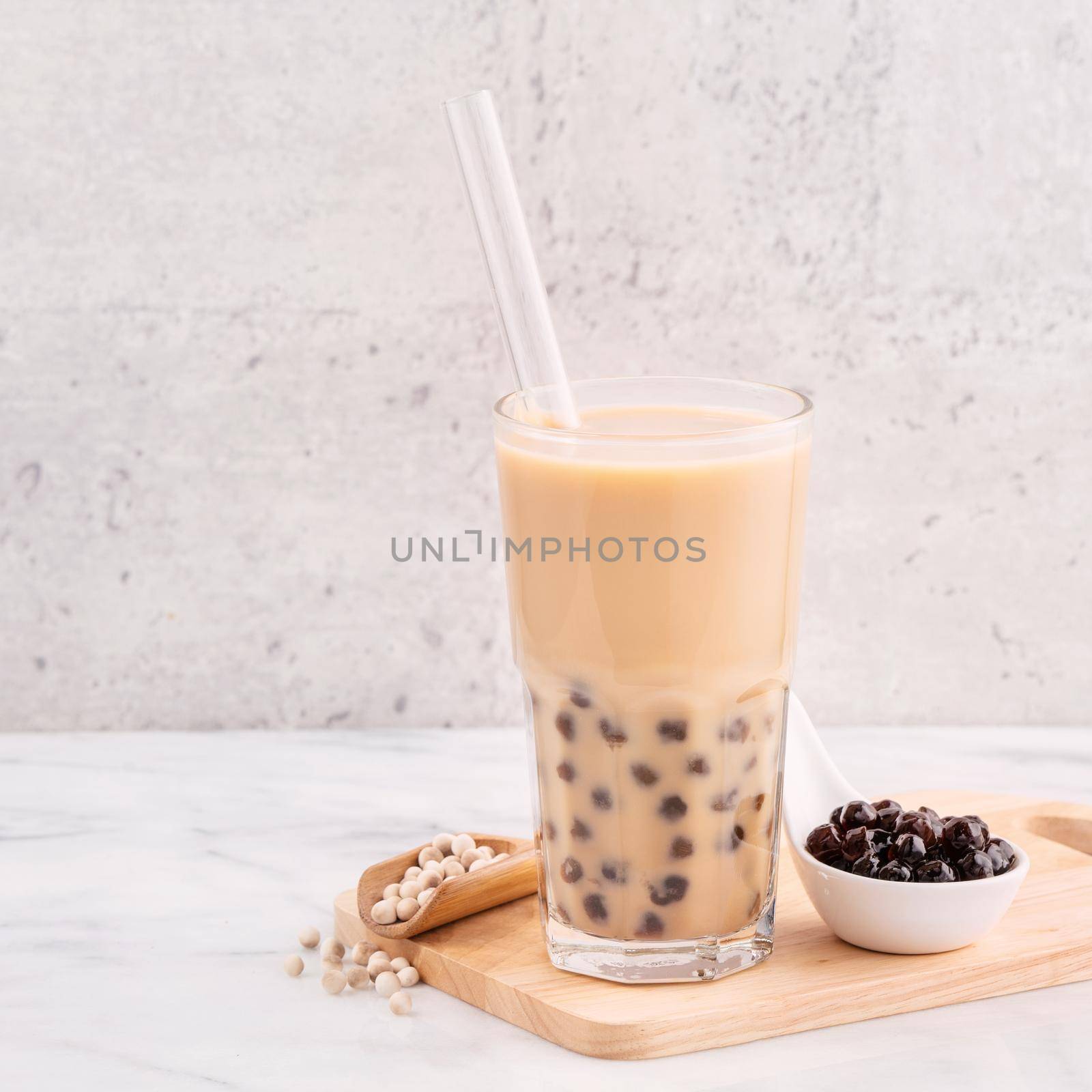 Tapioca pearl ball bubble milk tea, popular Taiwan drink, in drinking glass with straw on marble white table and wooden tray, close up, copy space.