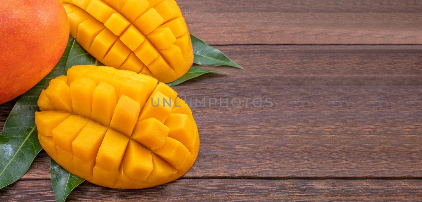 Fresh mango - beautiful chopped fruit with green leaves on dark wooden timber background. Tropical fruit design concept. Flat lay. Top view. Copy space