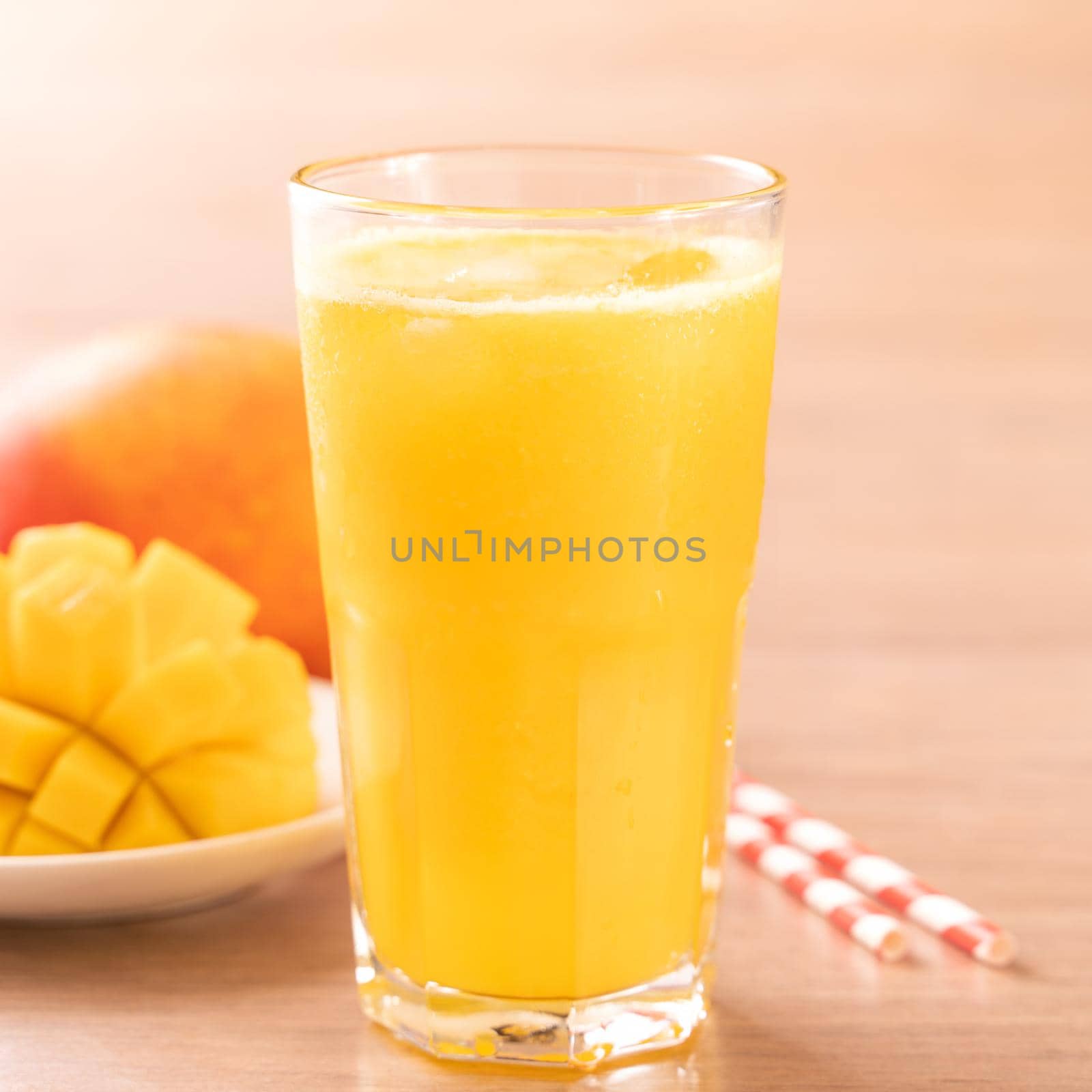 Fresh mango juice with beautiful chopped pulp flesh and straw on bright wooden table background. Tropical fruit design concept. Close up, copy space.