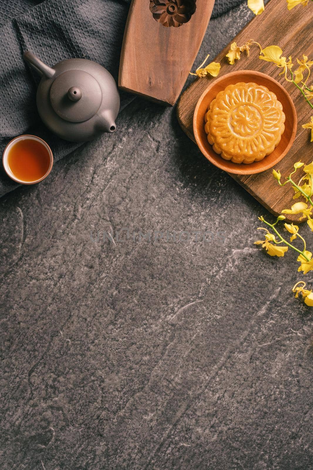 Mid-Autumn Festival traditional food concept - Beautiful Moon cake on black slate table with tea, pastry mold, flower, top view, flat lay, copy space
