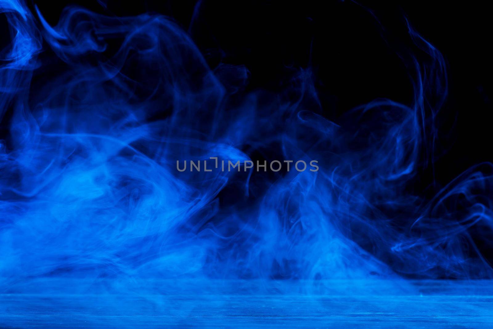 Conceptual image of blue smoke isolated on dark black background and wooden table.