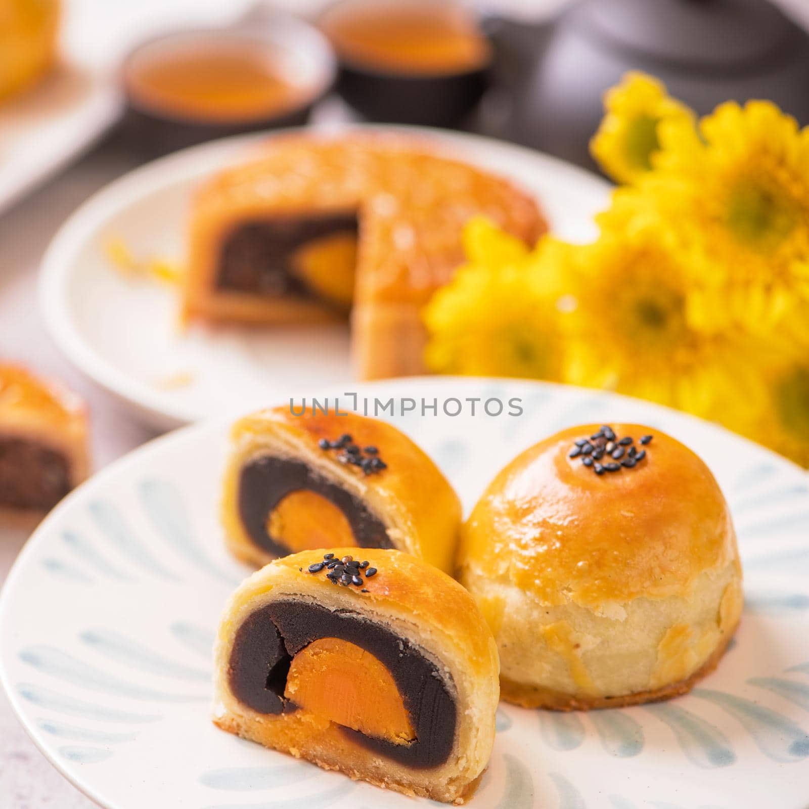 Mid-Autumn Festival traditional food concept - Beautiful cut moon cake on blue pattern plate on white background with flower, close up, copy space