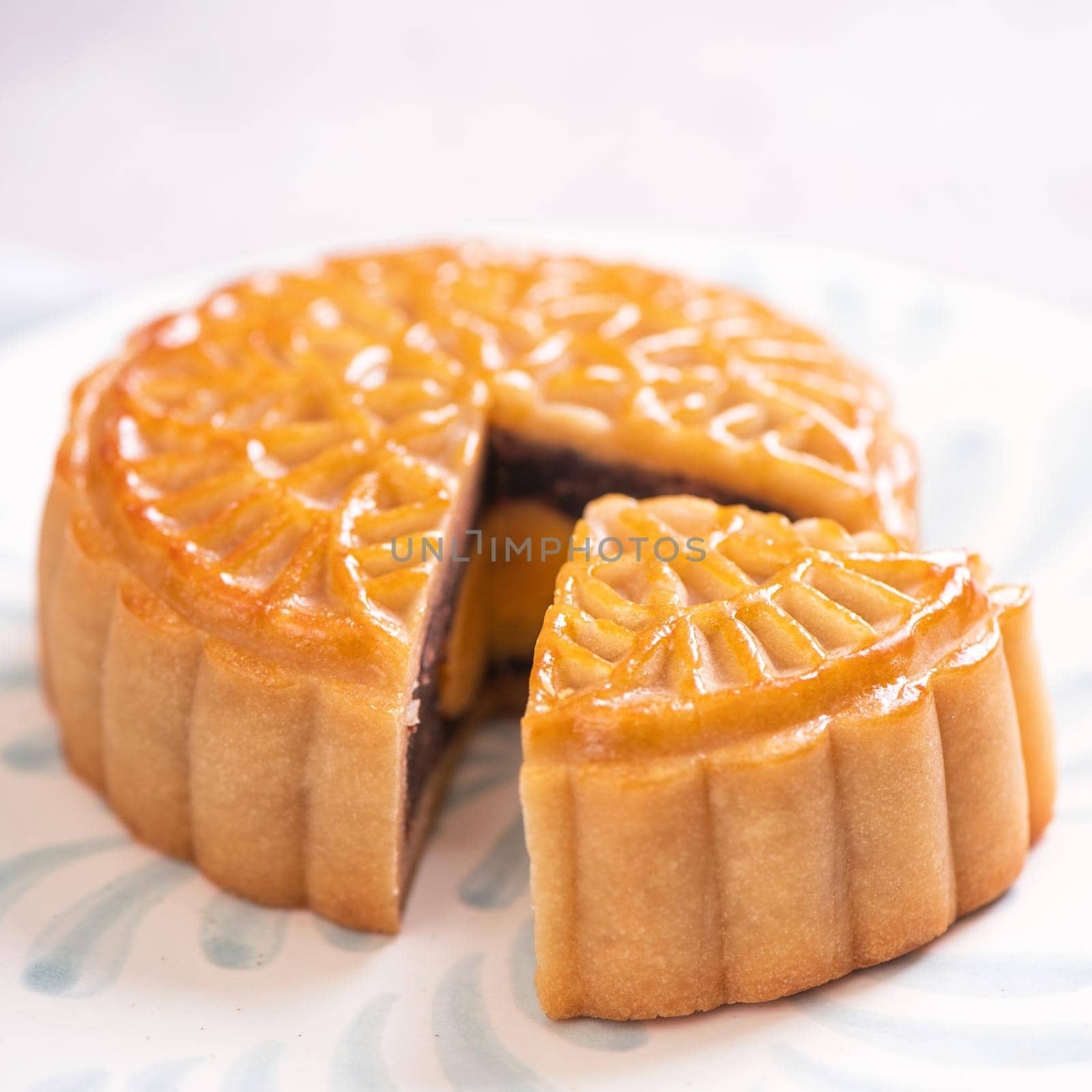 Mid-Autumn Festival traditional food concept - Beautiful cut moon cake on blue pattern plate on white background with flower, close up, copy space