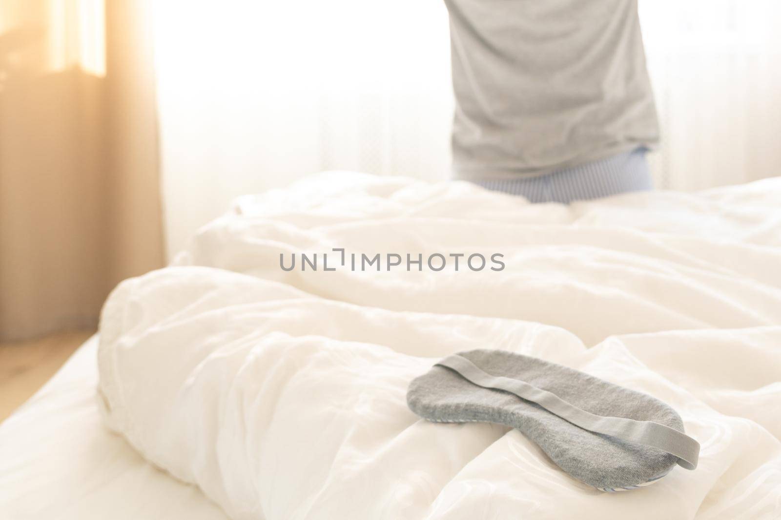 Sleeping mask on a bed with stretching woman in the background, back view