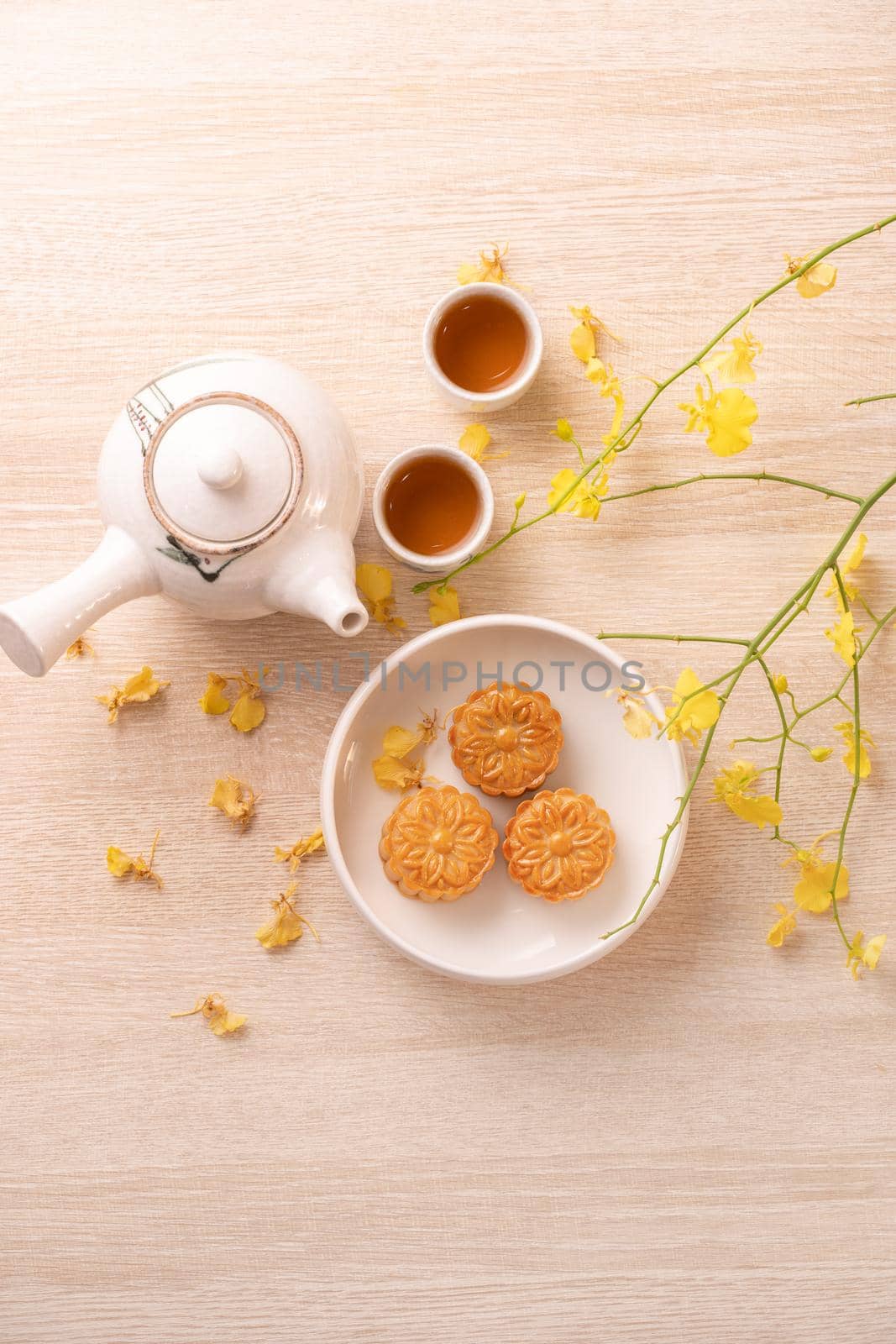 Tasty moon cake for Mid-Autumn festival on bright wooden table, concept of festive afternoon tea decorated with yellow flowers, top view, flat lay.