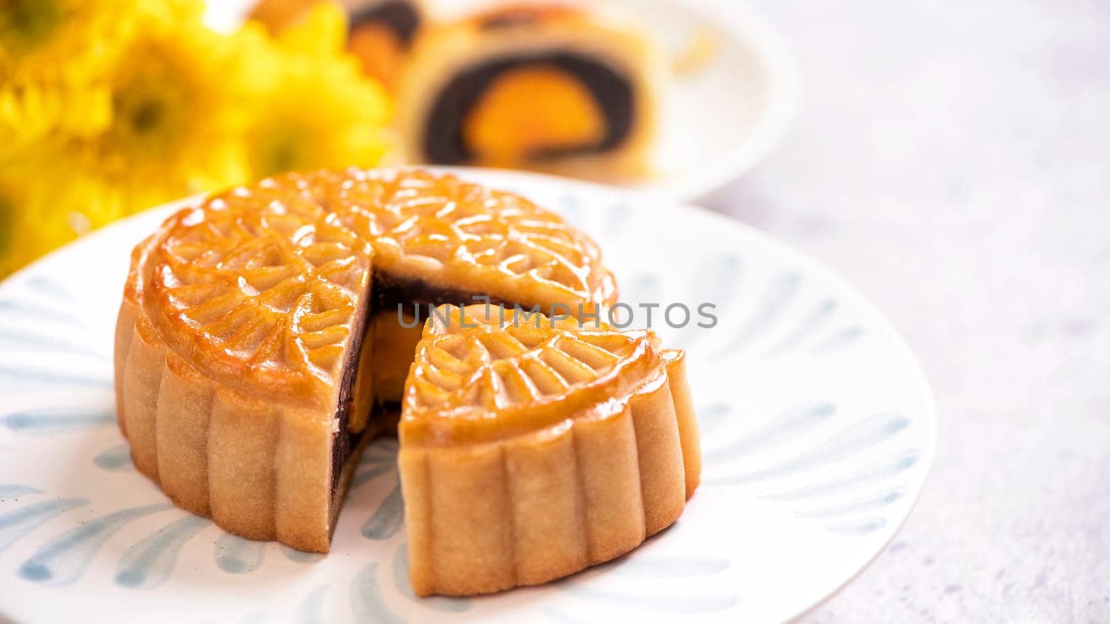 Mid-Autumn Festival traditional food concept - Beautiful cut moon cake on blue pattern plate on white background with flower, close up, copy space