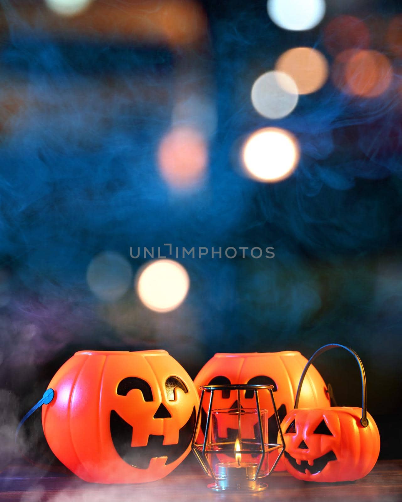 Halloween concept - Orange plastic pumpkin lantern on a dark wooden table with blurry sparkling light in the background, trick or treat, close up.