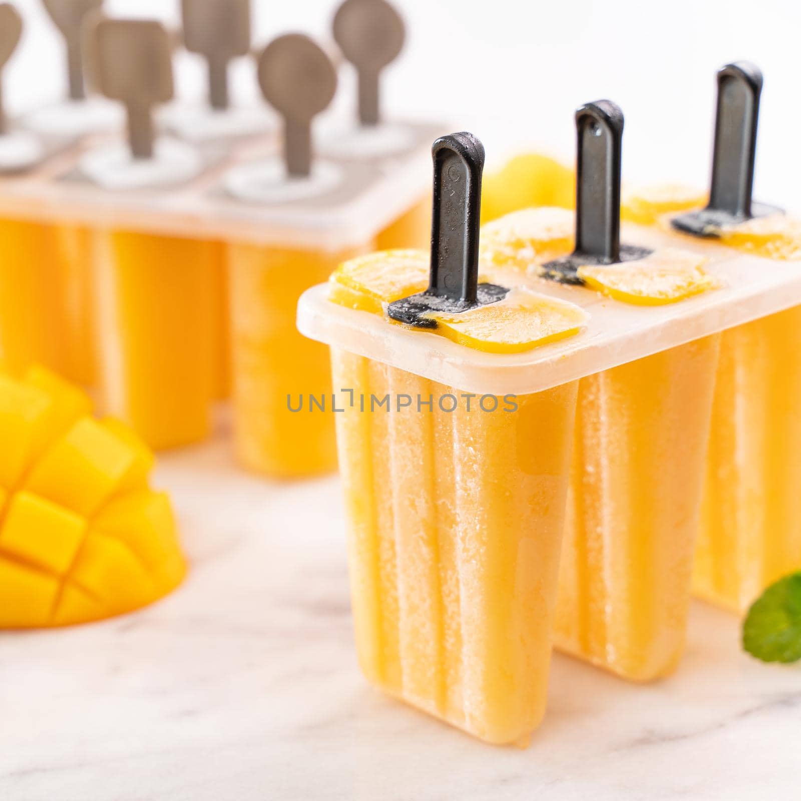 Fresh mango fruit popsicle ice in the plastic shaping box on bright marble table. Summer mood concept product design, close up.