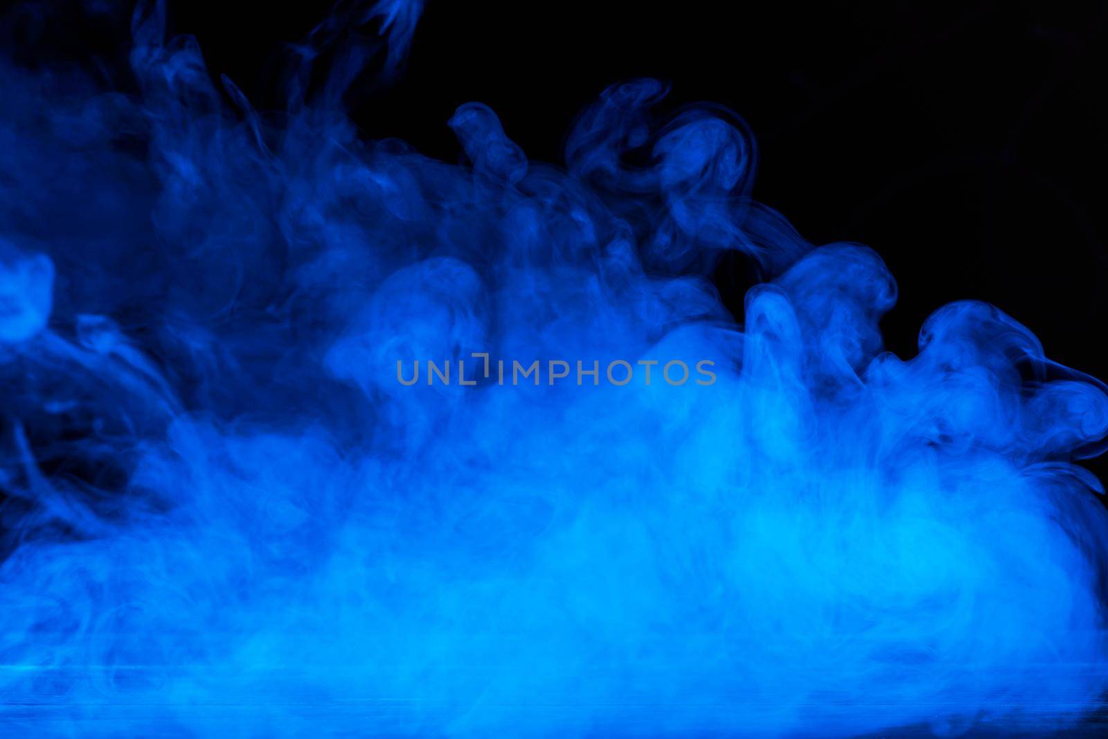 Conceptual image of blue smoke isolated on dark black background and wooden table.