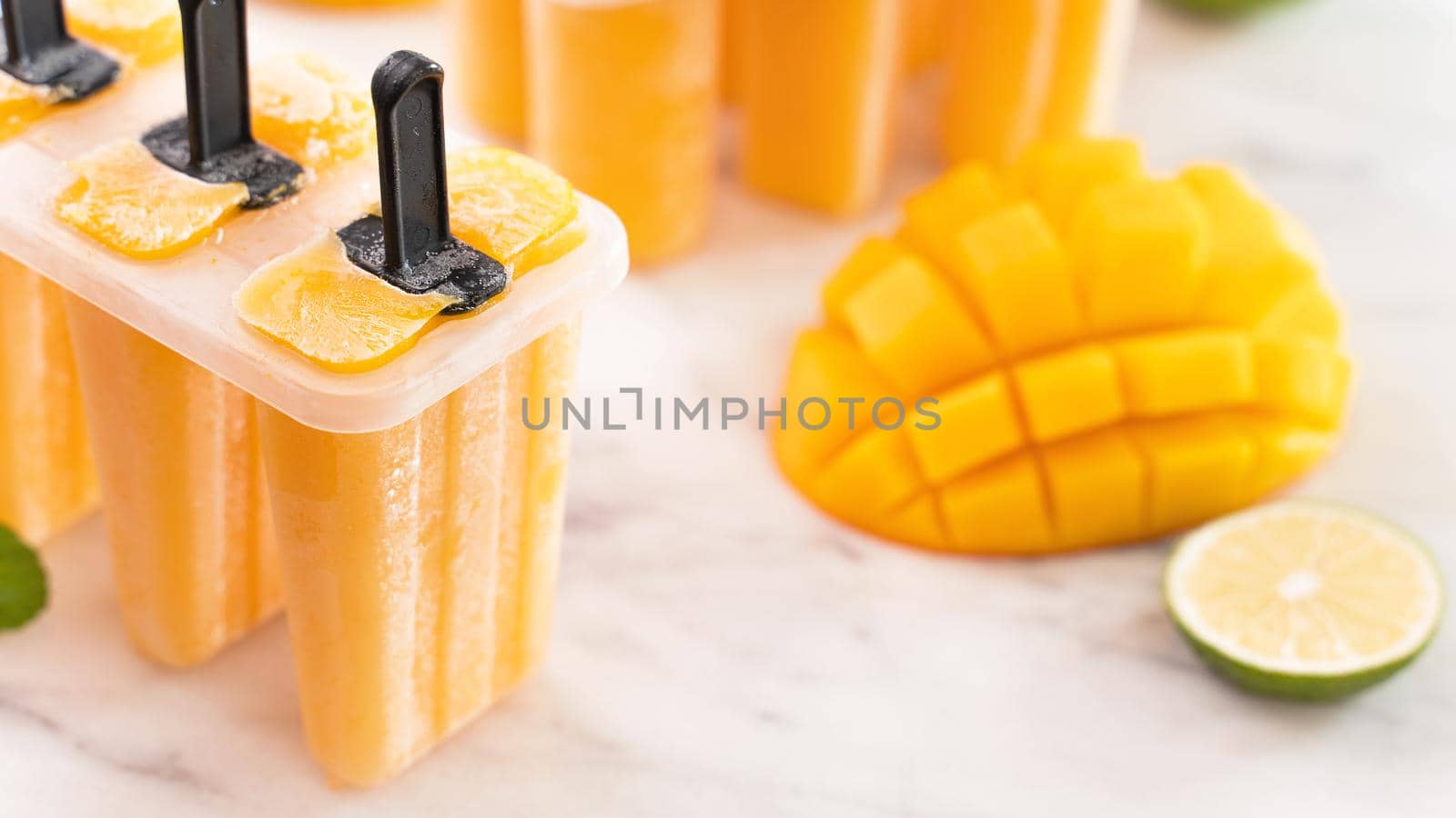 Fresh mango fruit popsicle ice in the plastic shaping box on bright marble table. Summer mood concept product design, close up.