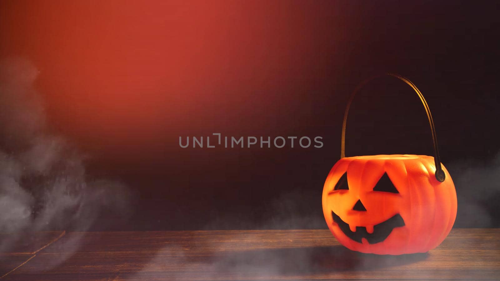 Halloween concept - Orange plastic pumpkin lantern on a dark wooden table with blurry sparkling light in the background, trick or treat, close up.