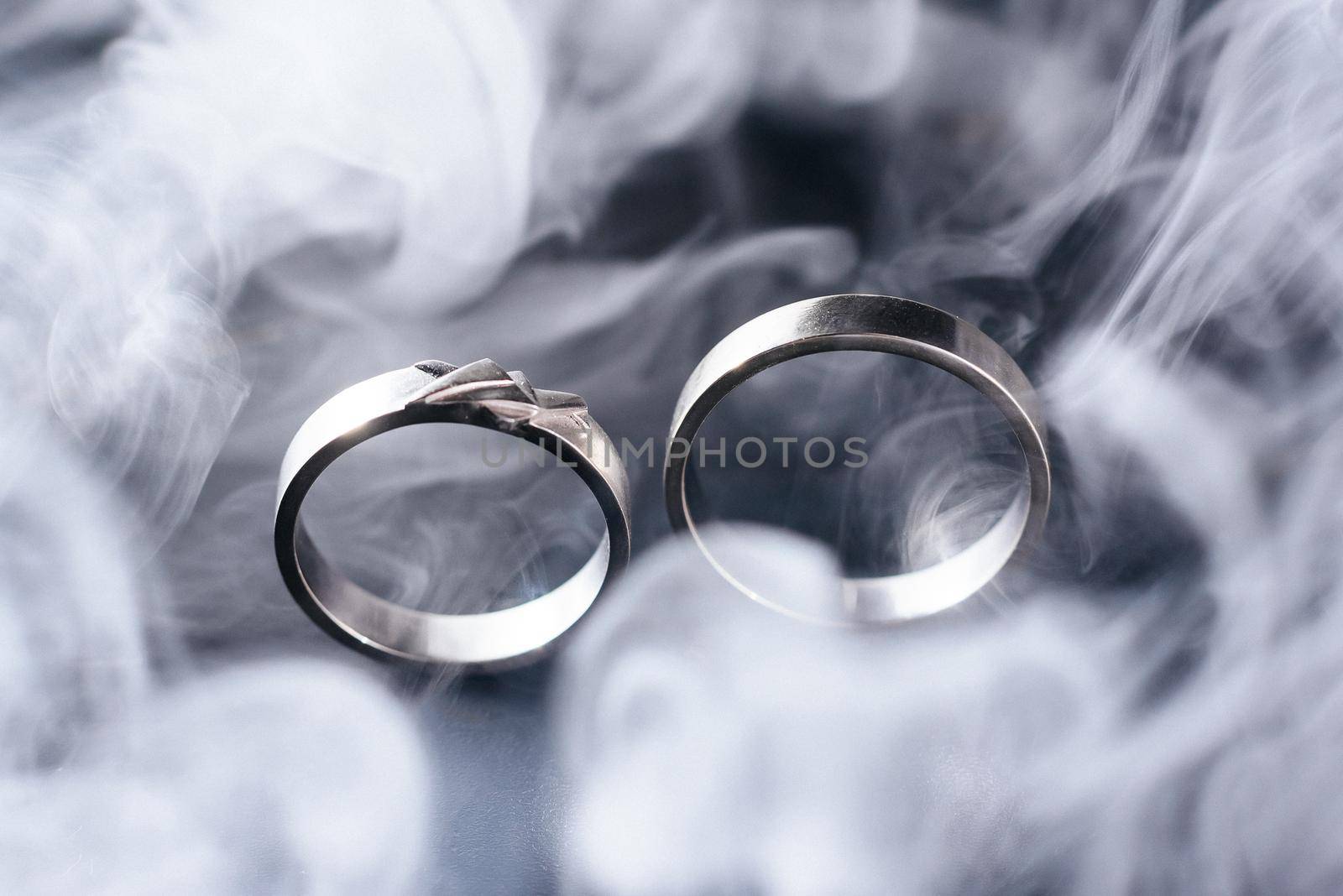 Two golden wedding rings with white smoke around, copy space and black background by Mariakray