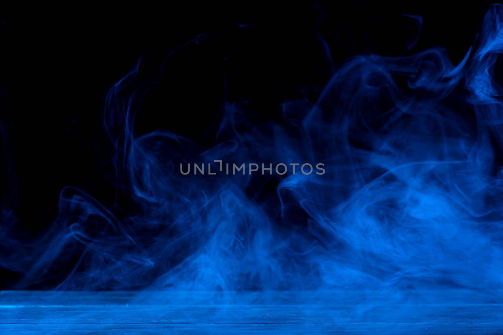 Conceptual image of blue smoke isolated on dark black background and wooden table.