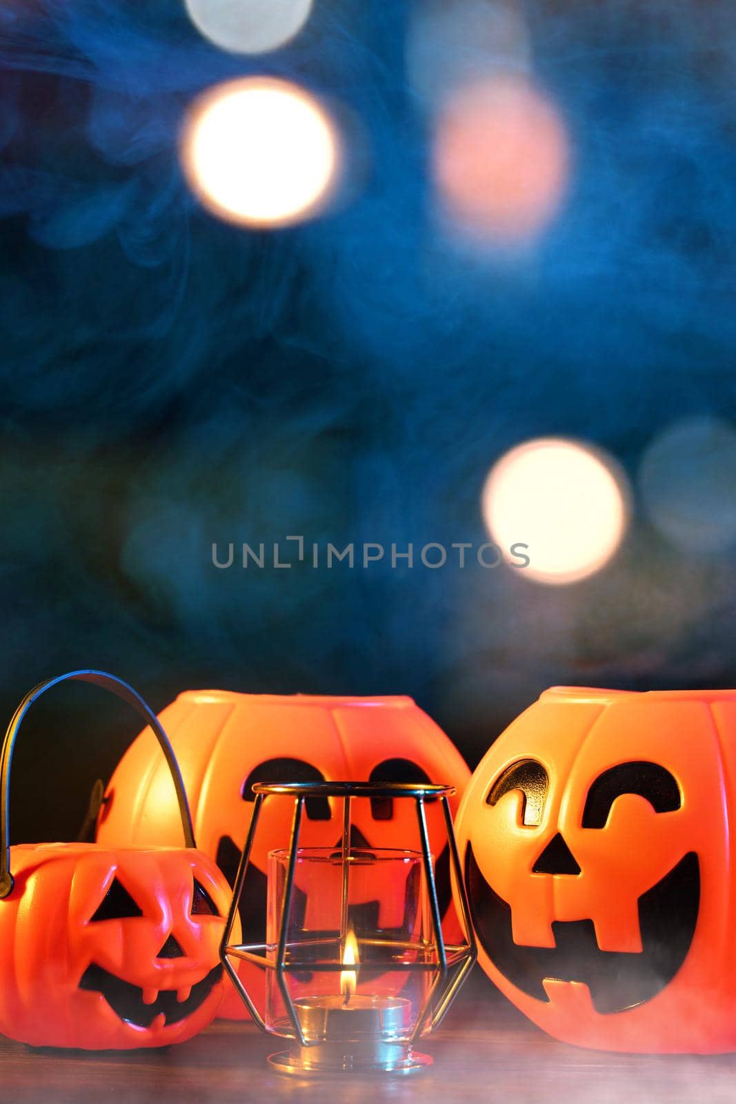 Halloween concept - Orange plastic pumpkin lantern on a dark wooden table with blurry sparkling light in the background, trick or treat, close up.