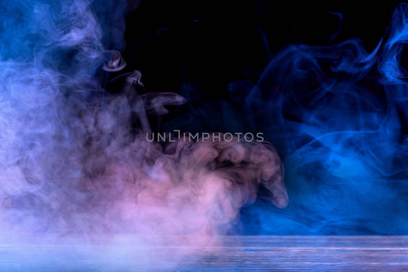 Conceptual image of multi-colored smoke isolated on dark black background and wooden table.
