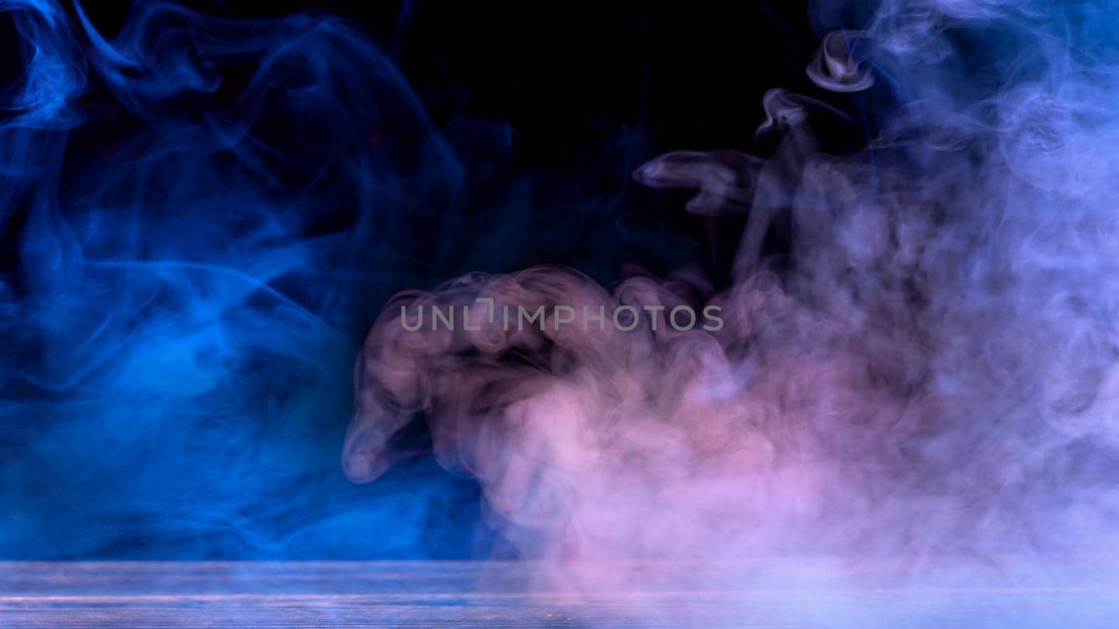 Conceptual image of multi-colored smoke isolated on dark black background and wooden table.