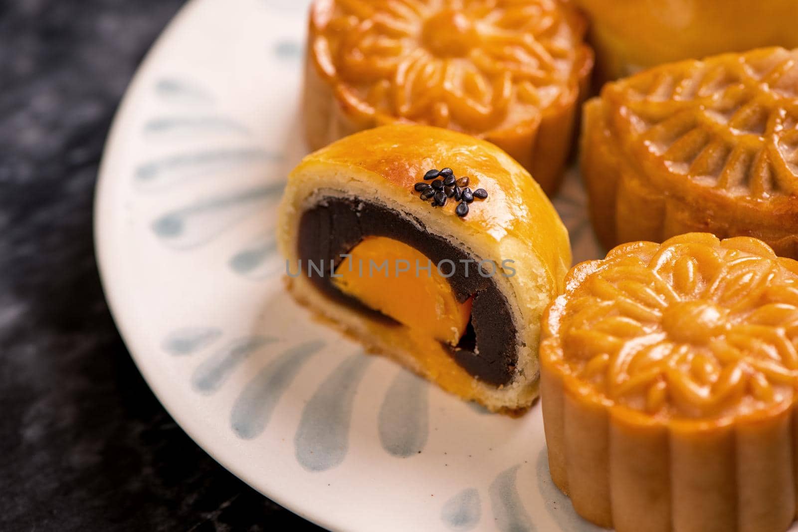 Tasty baked egg yolk pastry moon cake for Mid-Autumn Festival on black slate dark background. Chinese festive food concept, close up, copy space.