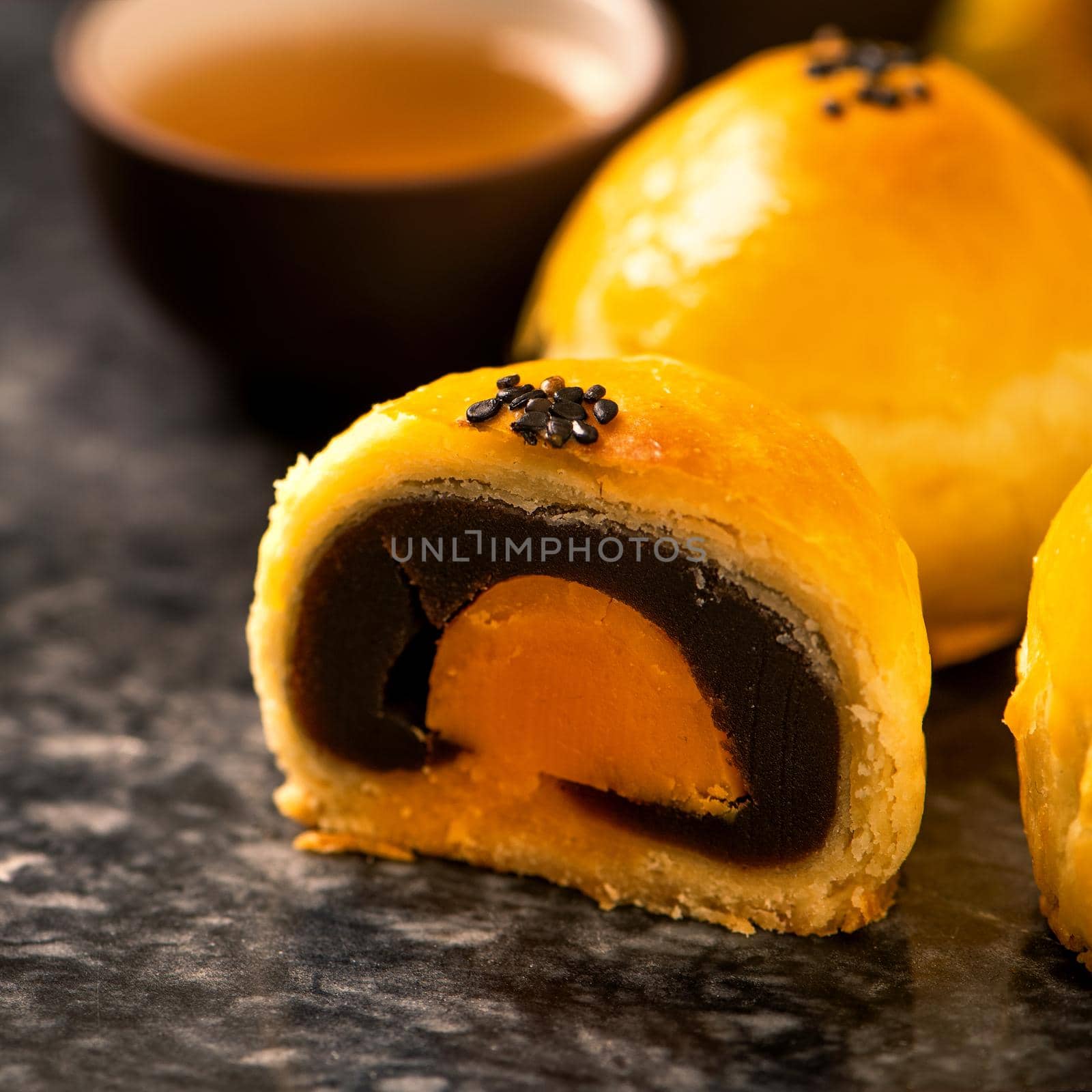 Tasty baked egg yolk pastry moon cake for Mid-Autumn Festival on black slate dark background. Chinese festive food concept, close up, copy space.
