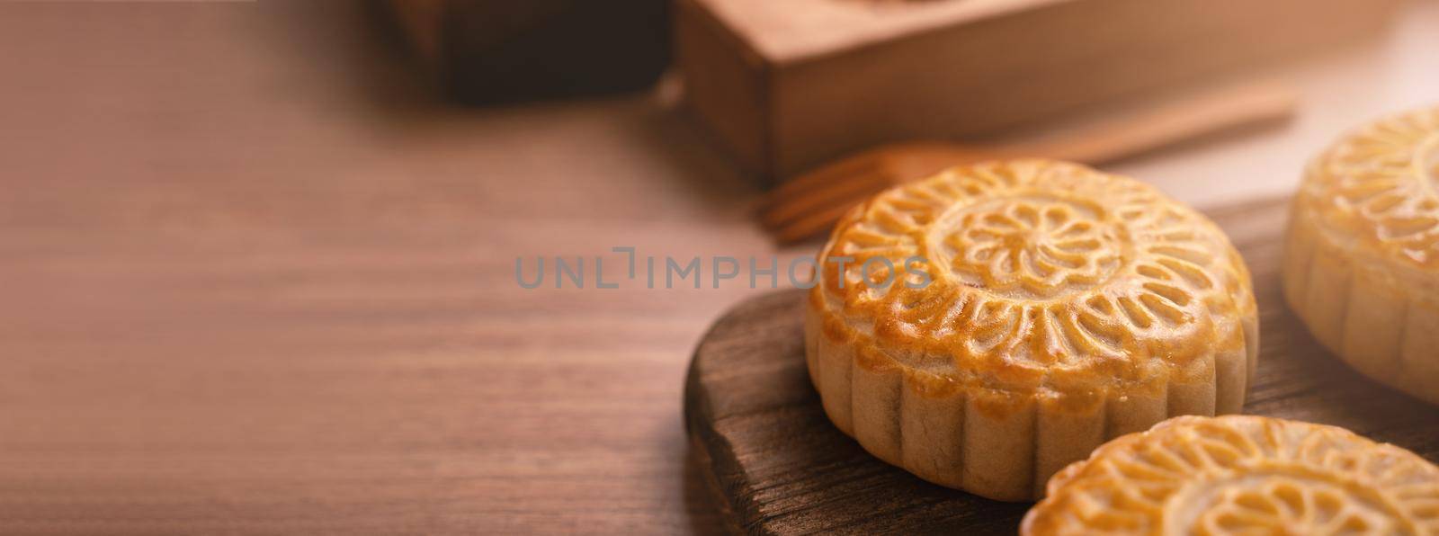 Round shaped fresh baked moon cake pastry - Chinese moonckae for Mid-Autumn Moon Festival on wooden background and serving tray, close up, copy space by ROMIXIMAGE