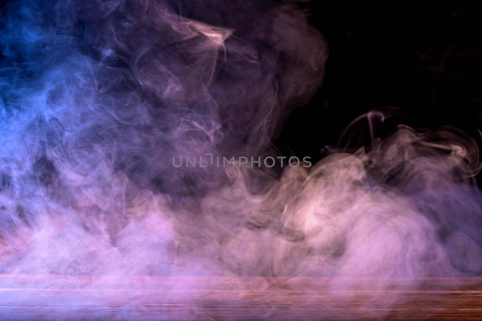 Conceptual image of multi-colored smoke isolated on dark black background and wooden table.
