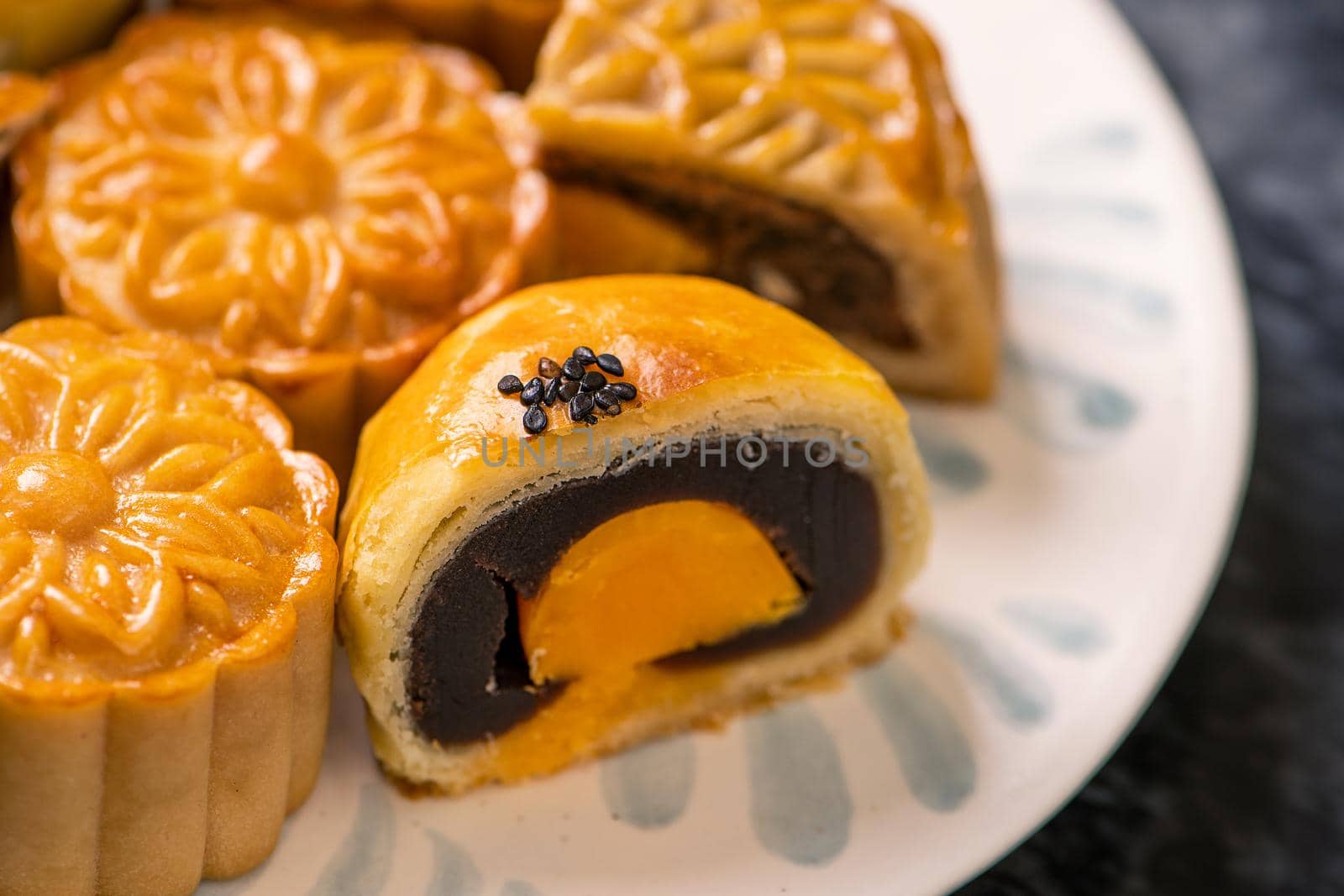 Tasty baked egg yolk pastry moon cake for Mid-Autumn Festival on black slate dark background. Chinese festive food concept, close up, copy space.