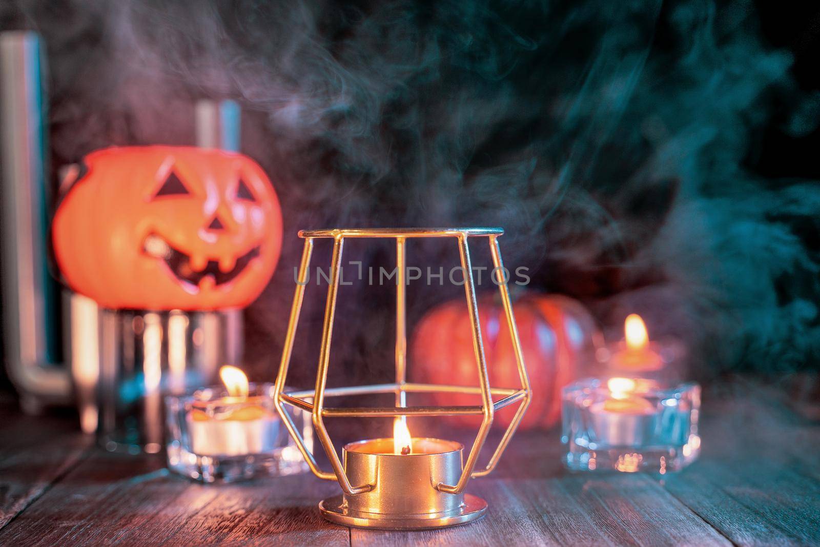 Halloween concept, orange pumpkin lantern and candles on a dark wooden table with green-orange smoke around the background, trick or treat, close up
