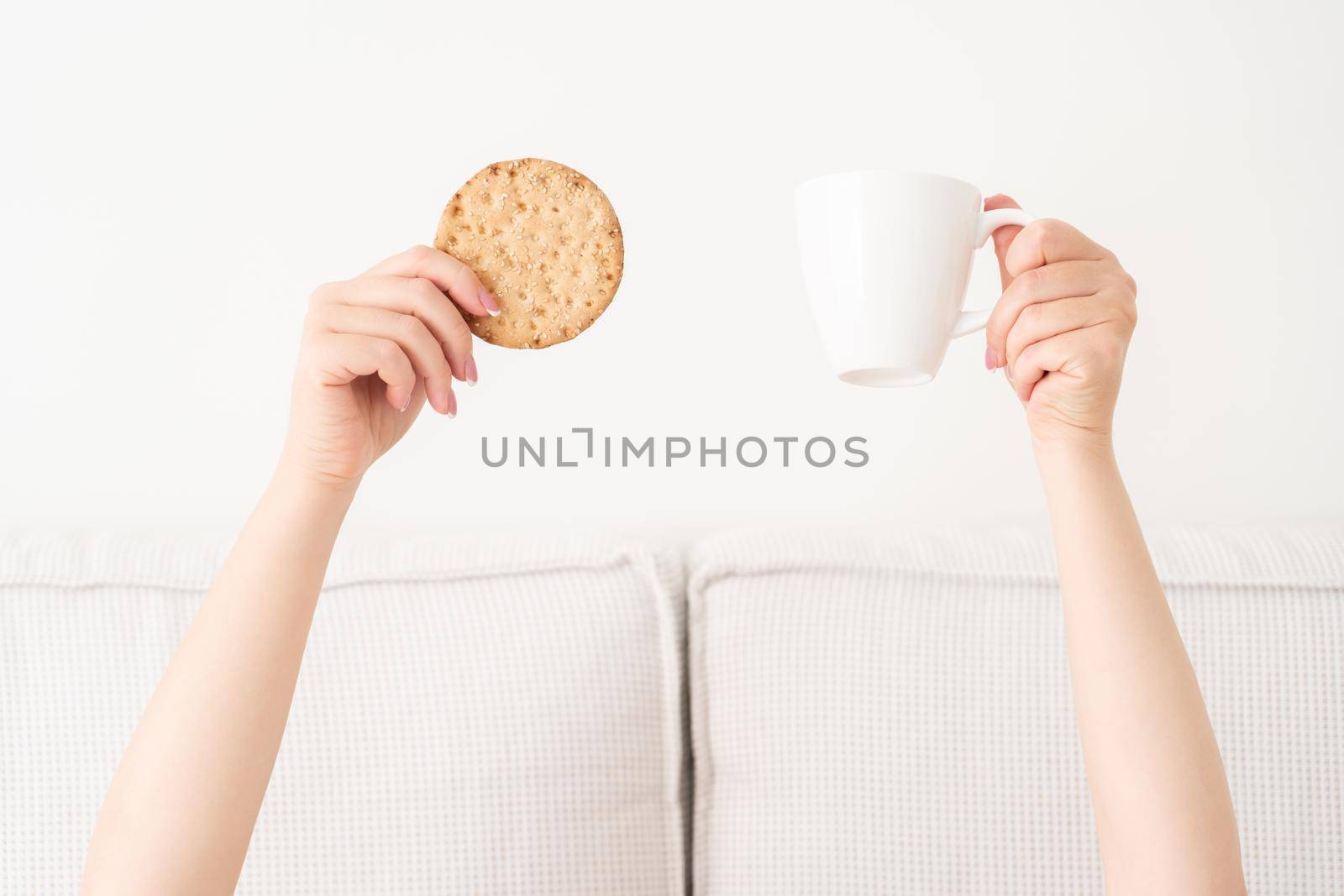 Female hand holding cup of coffee from under a blanket in bed. Woman waking up in the morning.