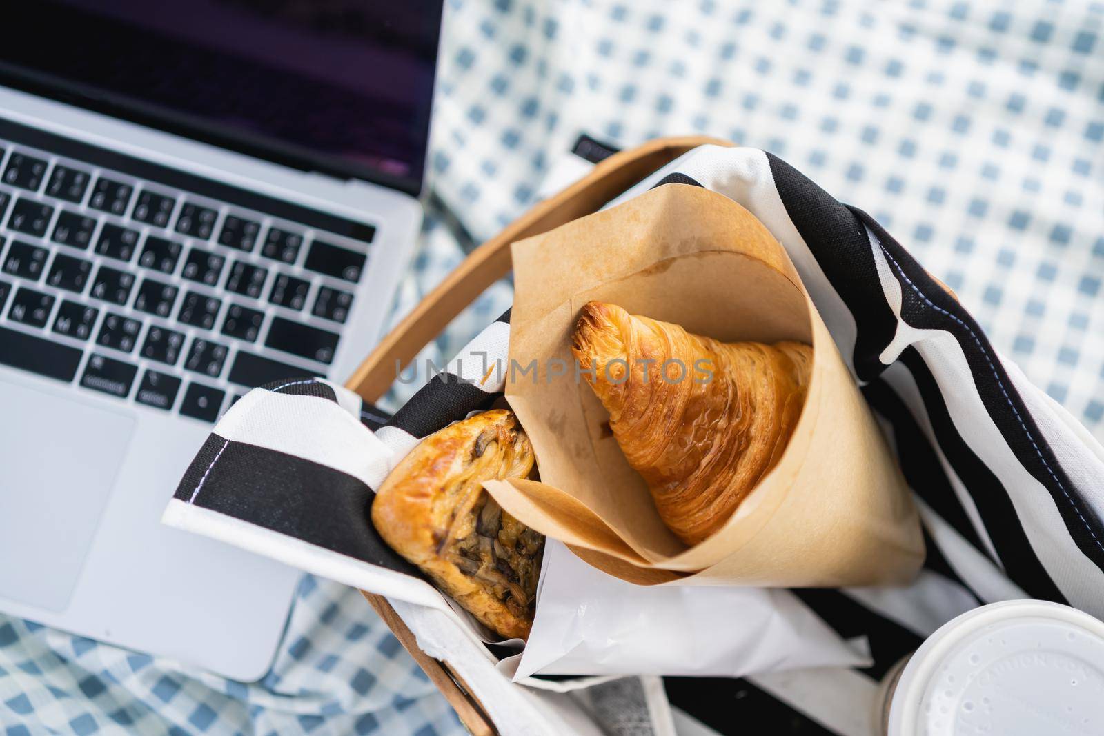 Croissant and laptop on the picnic table by Wmpix