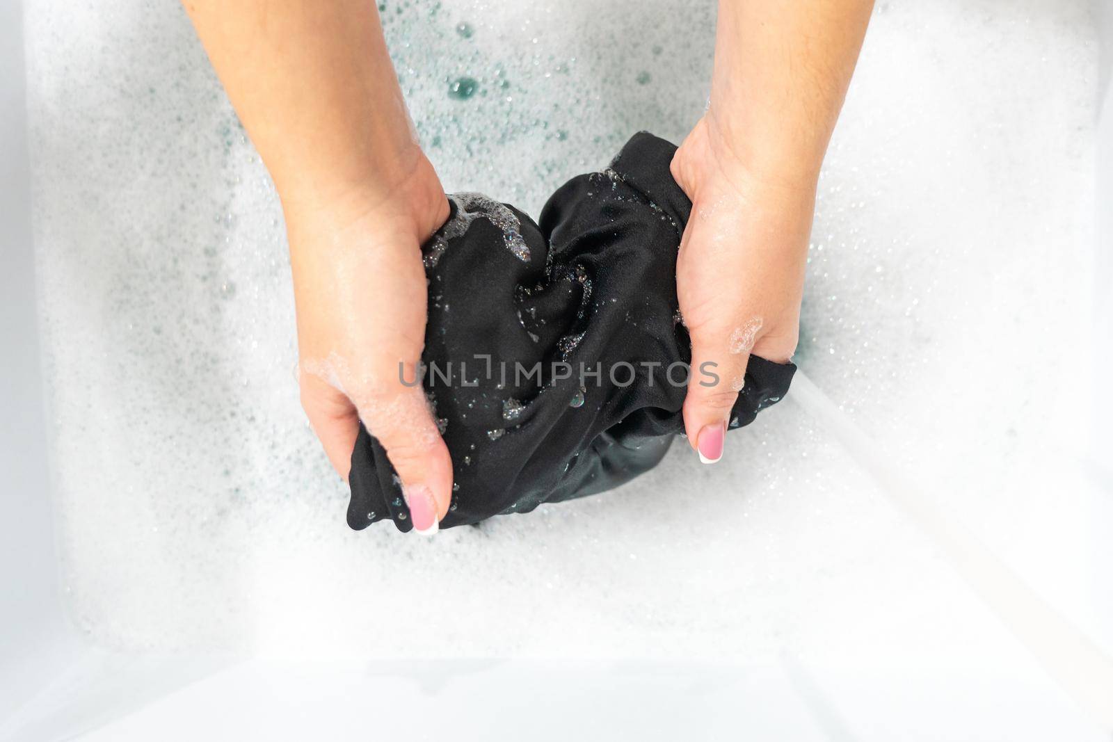 Female hands washing black color silk clothes in basin by Mariakray