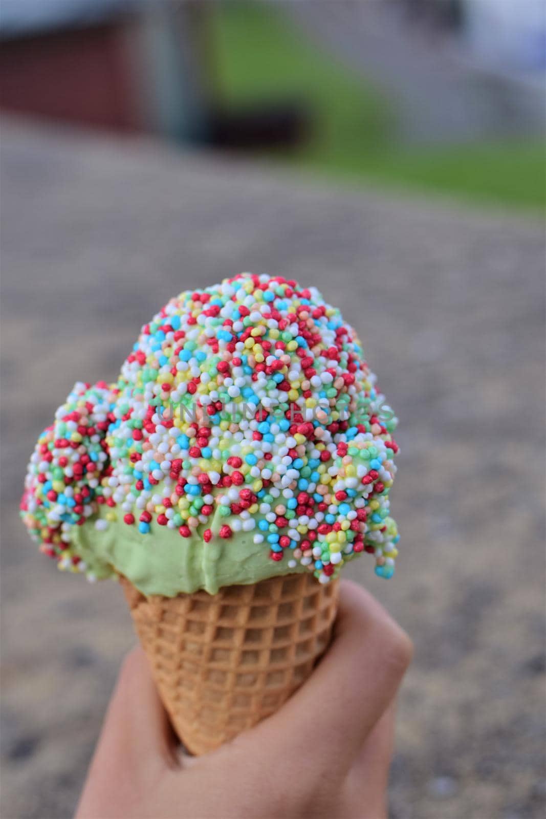 Ice cream with colorful sugar sprinkles in hand as a close-up against a blurred background