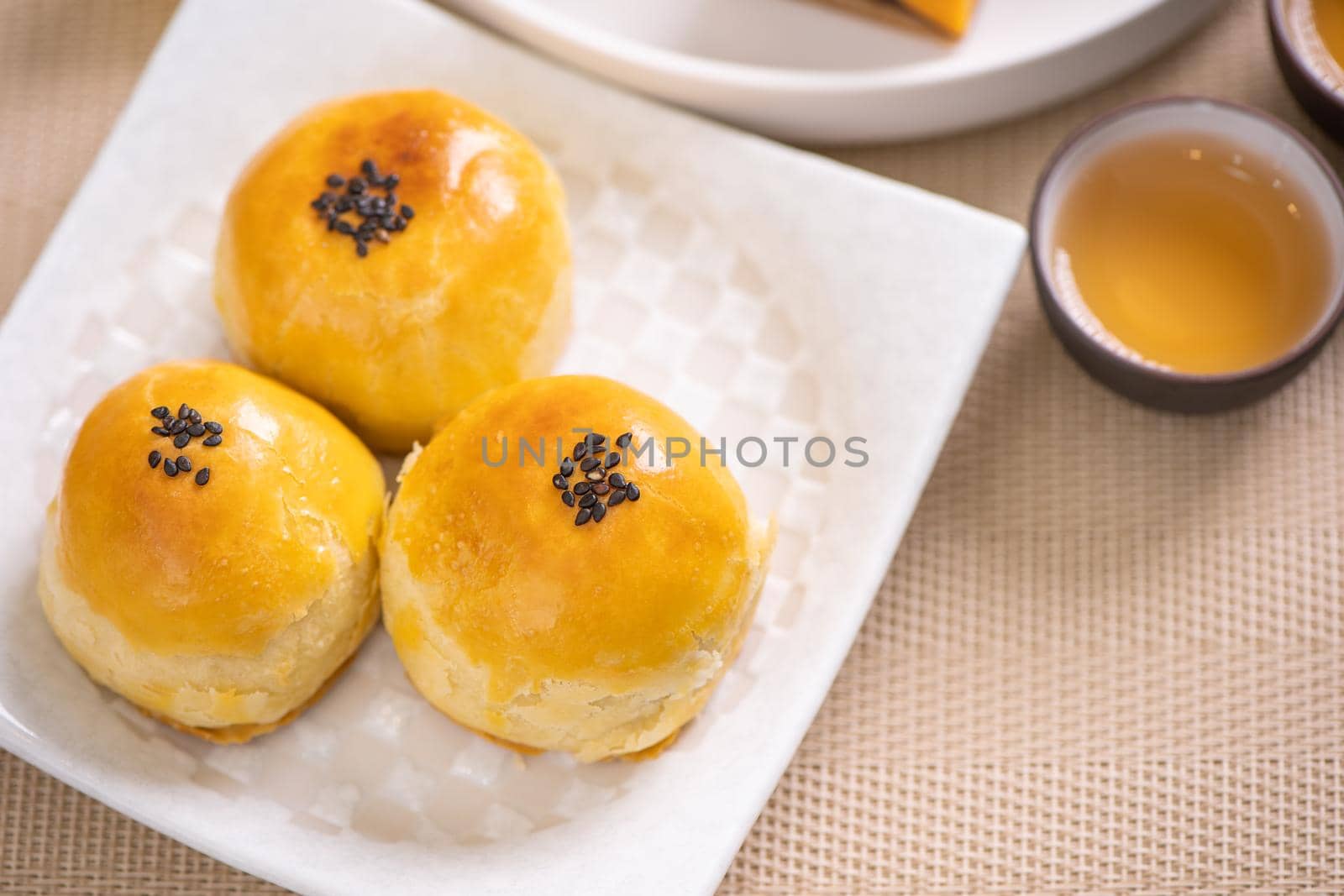 Mid-Autumn Festival traditional food concept - Beautiful cut moon cake on blue pattern plate on white background with flower, close up, copy space