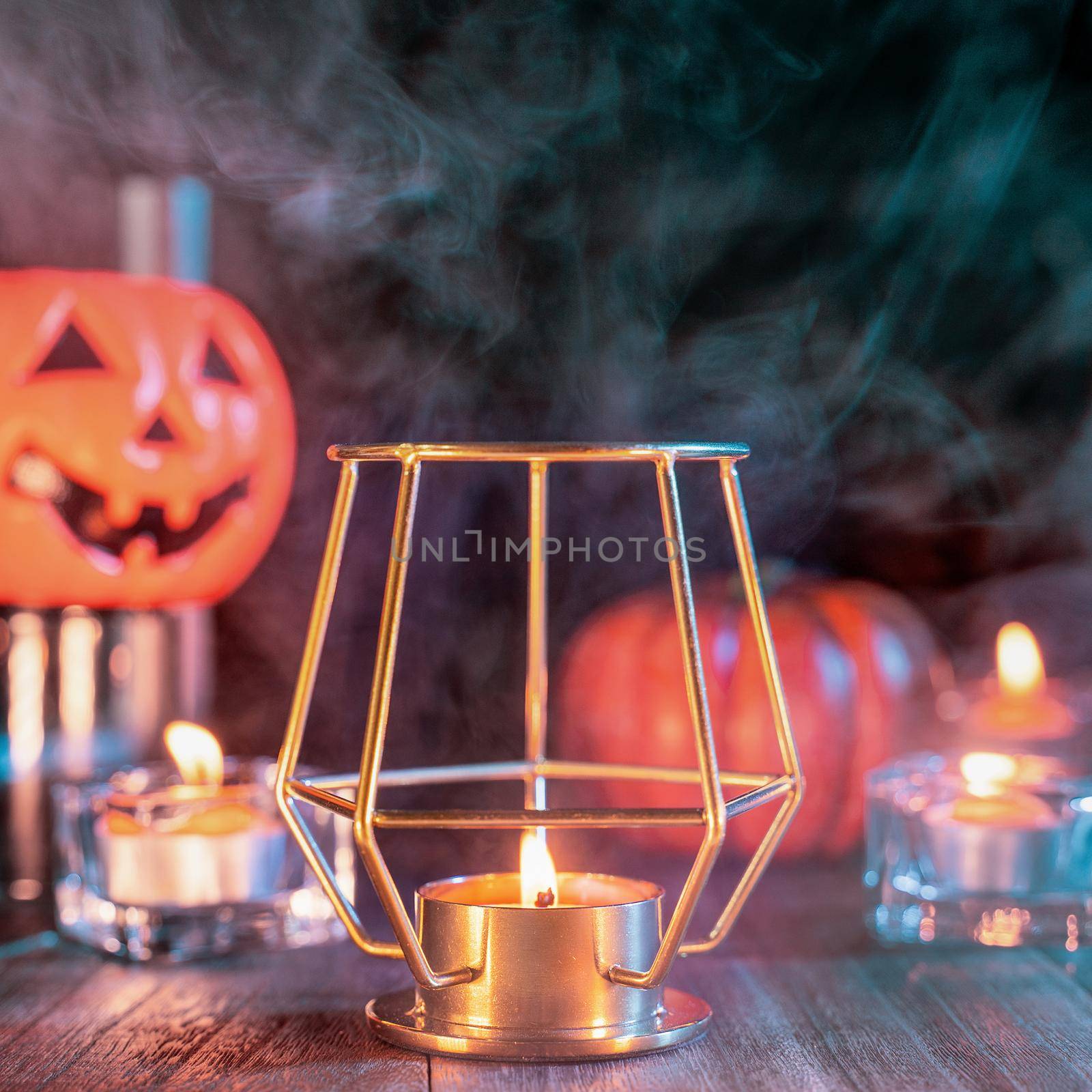 Halloween concept, orange pumpkin lantern and candles on a dark wooden table with green-orange smoke around the background, trick or treat, close up
