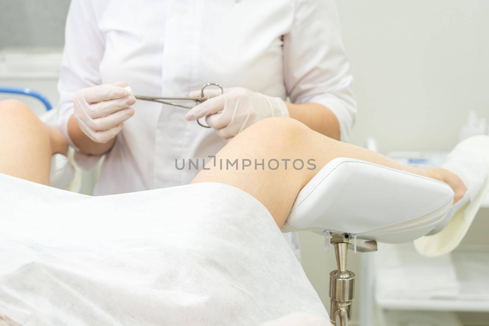 Gynecology doctor examining female patient on gynecological chair holding forceps by Mariakray