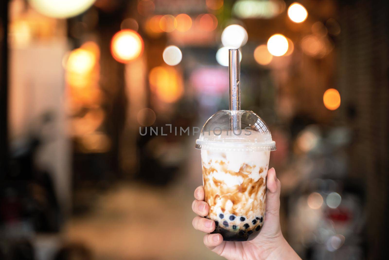 Young girl in denim jacket is drinking brown sugar flavored tapioca pearl bubble milk tea with glass straw in night market of Taiwan, close up, bokeh