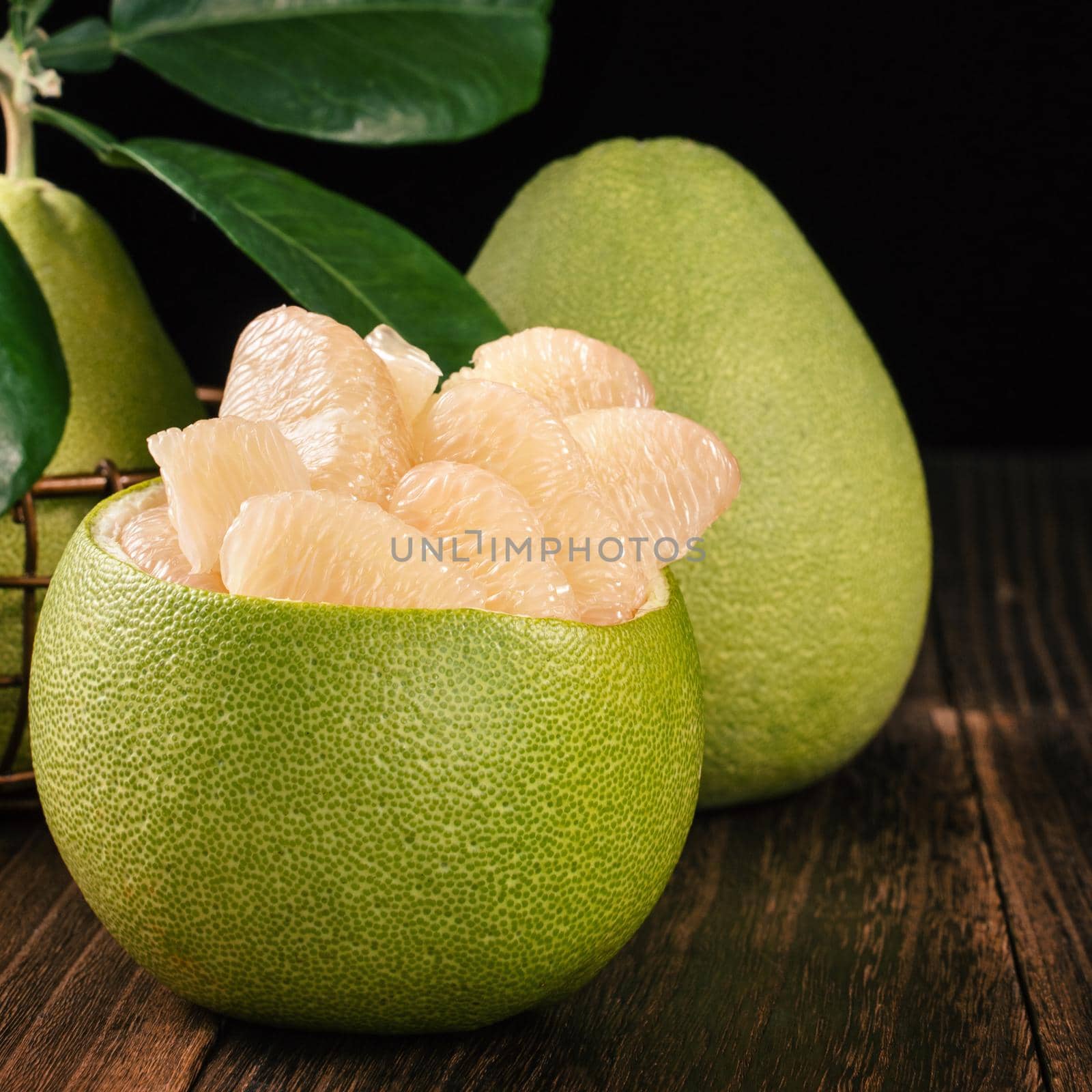 Fresh peeled pomelo, grapefruit, shaddock with green leaves on dark wooden plank table. Seasonal fruit near mid-autumn festival, close up, copy space