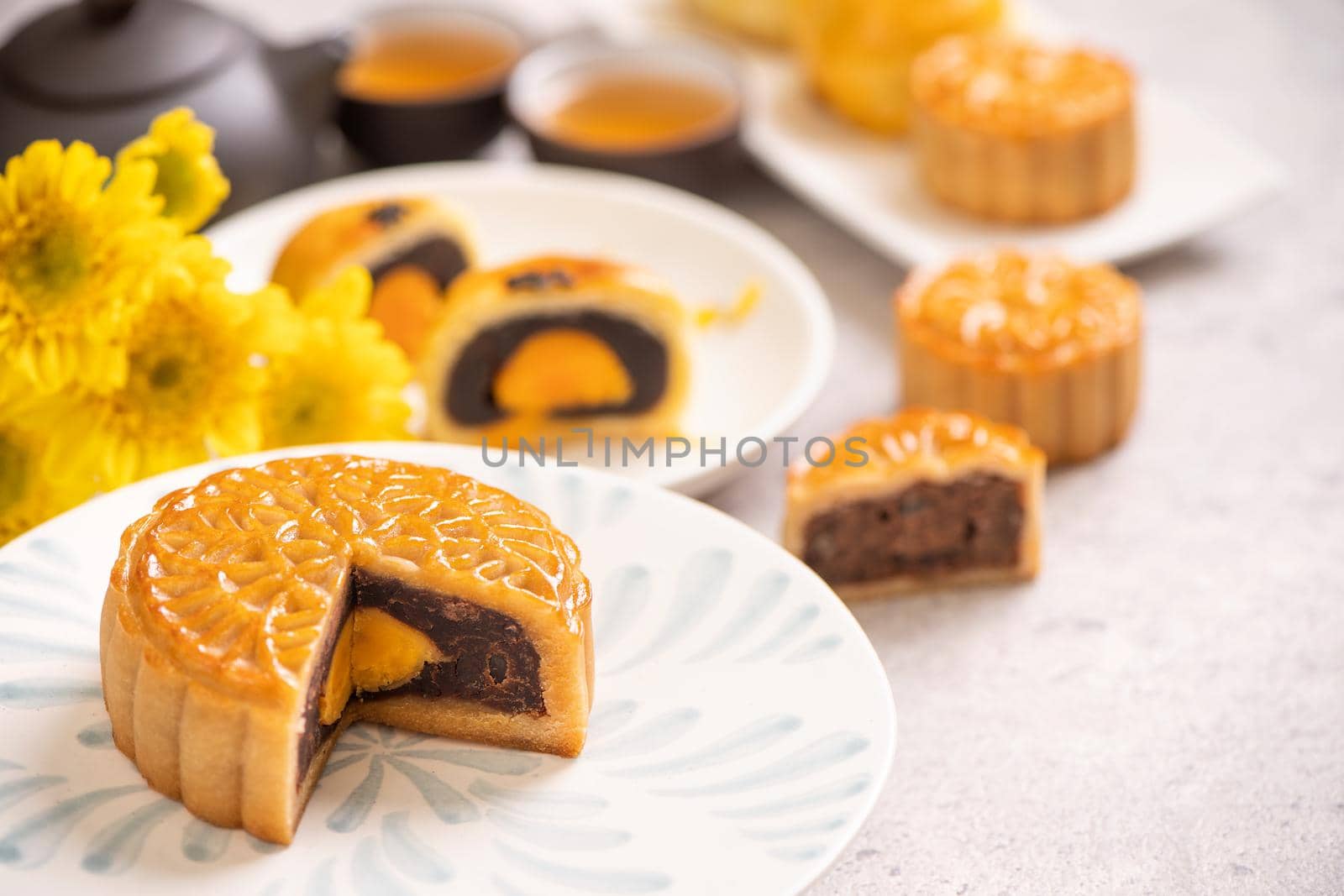 Mid-Autumn Festival traditional food concept - Beautiful cut moon cake on blue pattern plate on white background with flower, close up, copy space