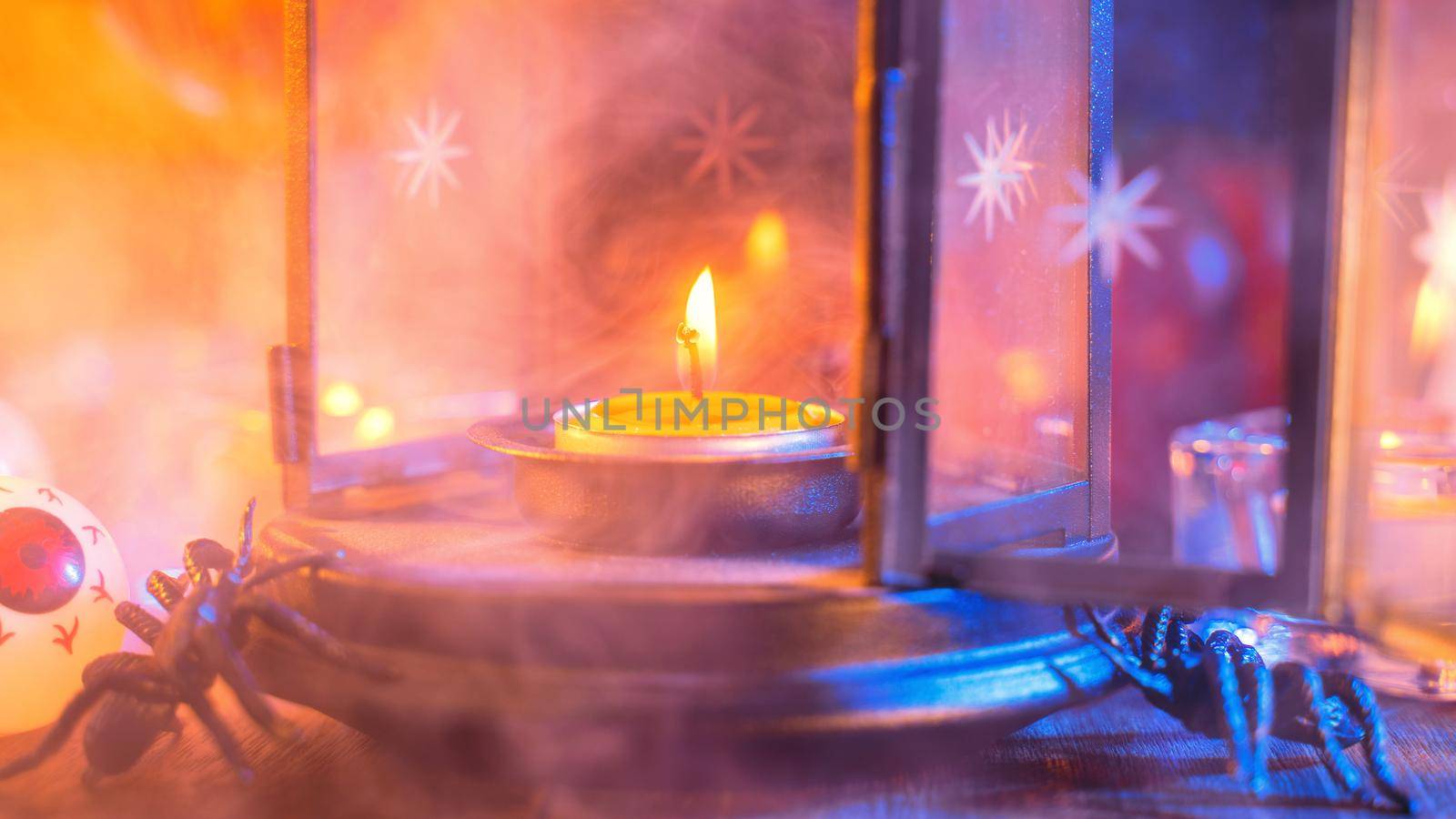 Halloween concept, spooky decorations with lighting up candle and candle holder with blue tone smoke around on a dark wooden table, close up.