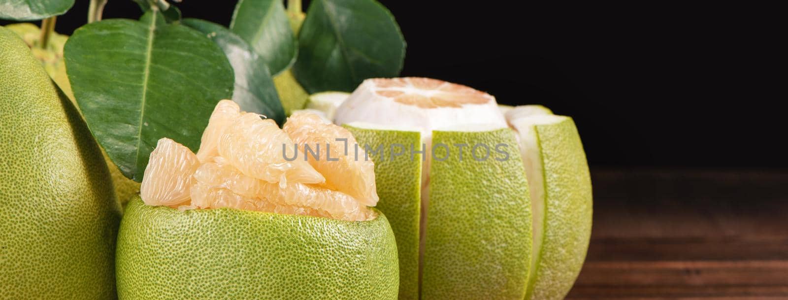 Fresh peeled pomelo, grapefruit, shaddock with green leaves on dark wooden plank table. Seasonal fruit near mid-autumn festival, close up, copy space