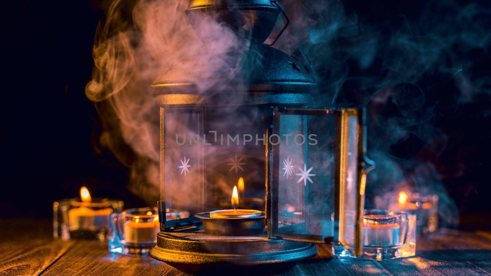 Halloween concept, spooky decorations with lighting up candle and candle holder with green tone smoke around on a dark wooden table, close up.