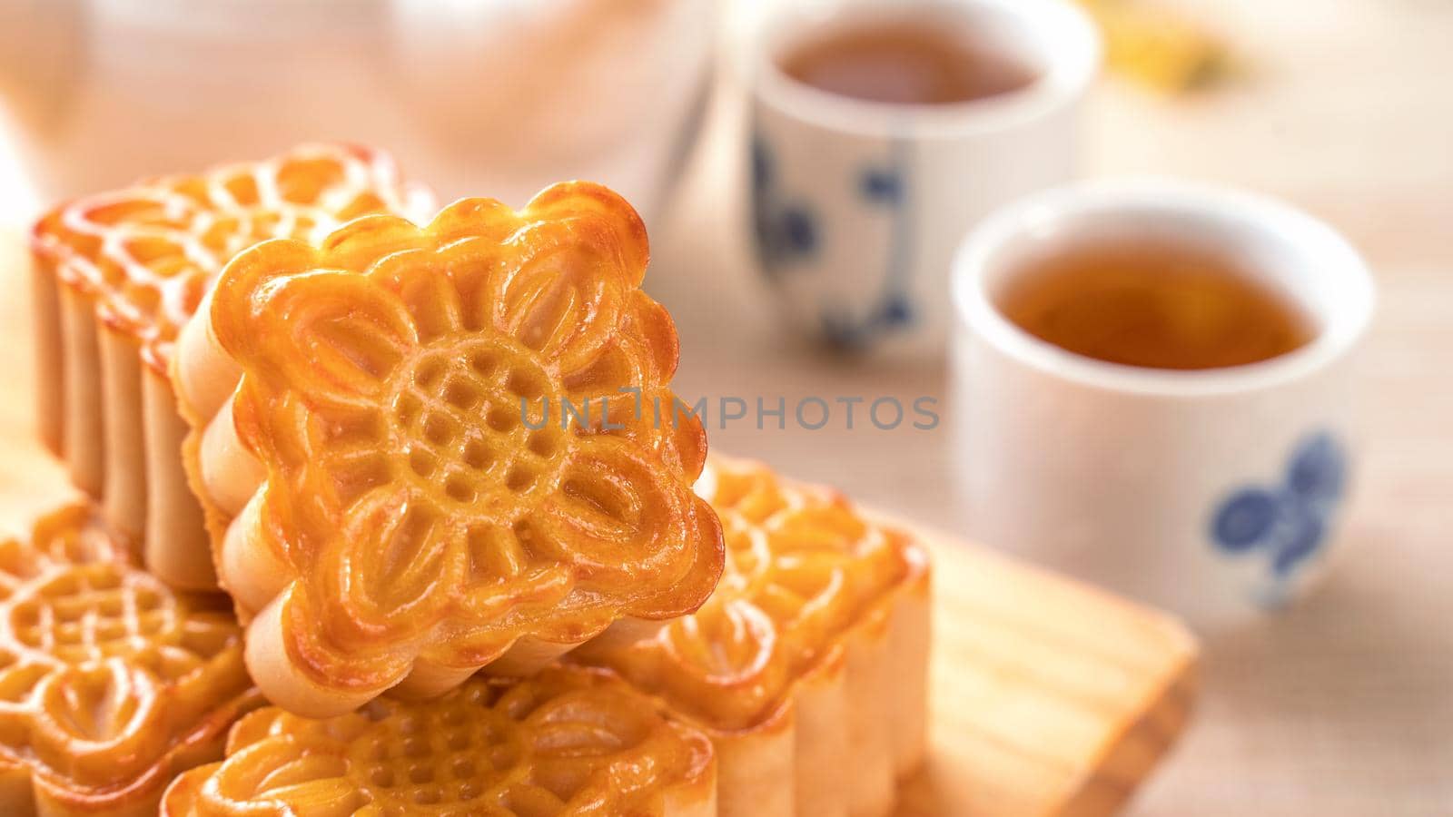 Moon cakes with tea on bright wooden table and serving try, holiday concept of Mid-Autumn festival traditional food layout design, close up, copy space.