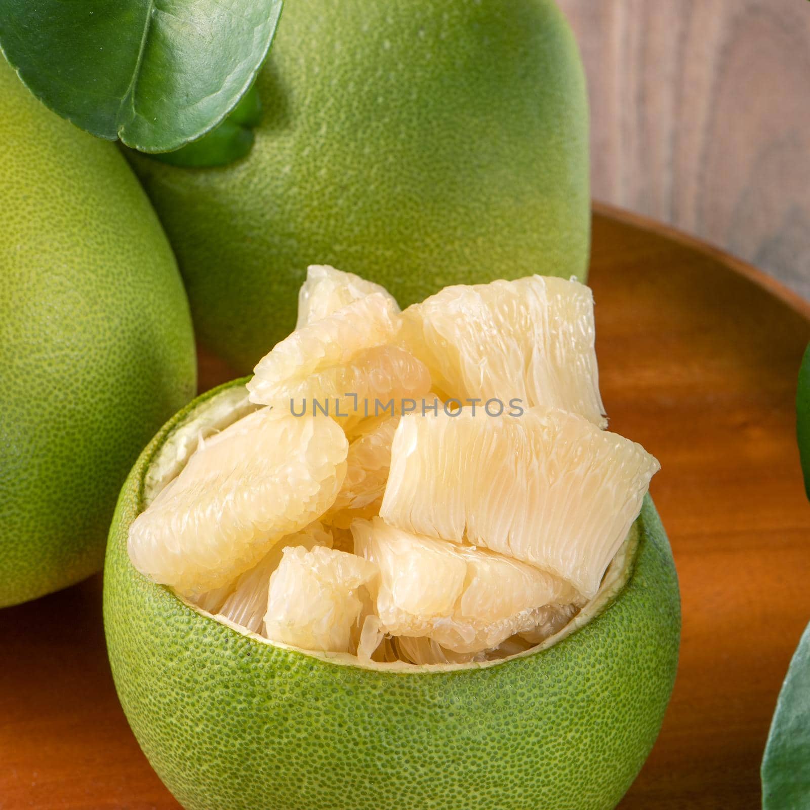 Fresh peeled pomelo, grapefruit, shaddock with green leaves on dark wooden plank table. Seasonal fruit near mid-autumn festival, close up, copy space