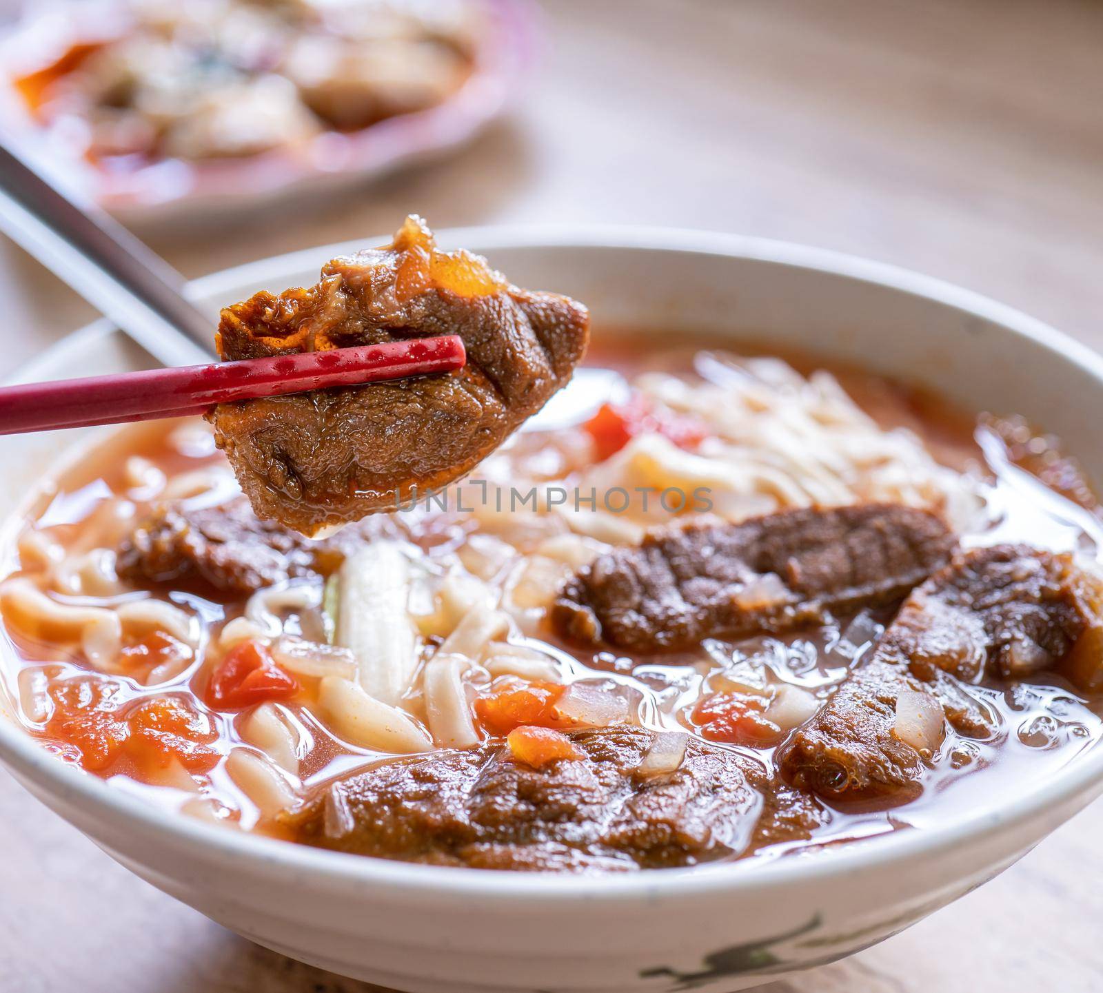 Beef noodle - Taiwan ramen meal with tomato sauce broth in bowl on bright wooden table, famous chinese style food, close up, top view, copy space